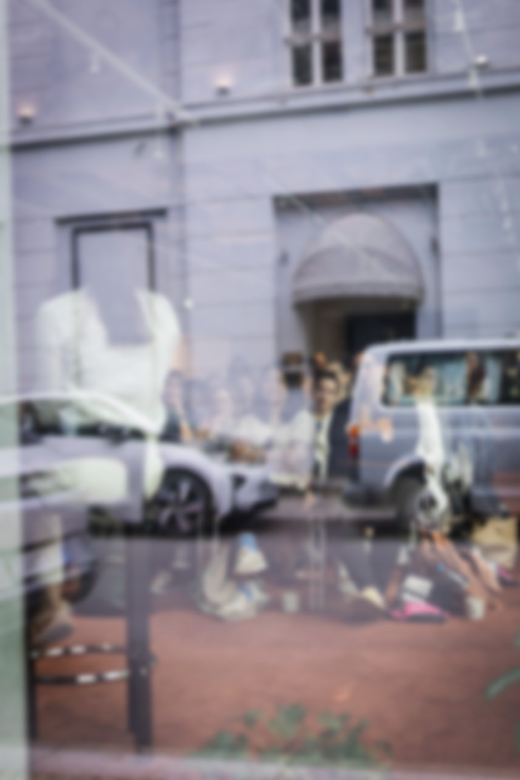 Reflected image of people walking outside, cars parked on the street, and a building with an arched doorway, seen through a window.