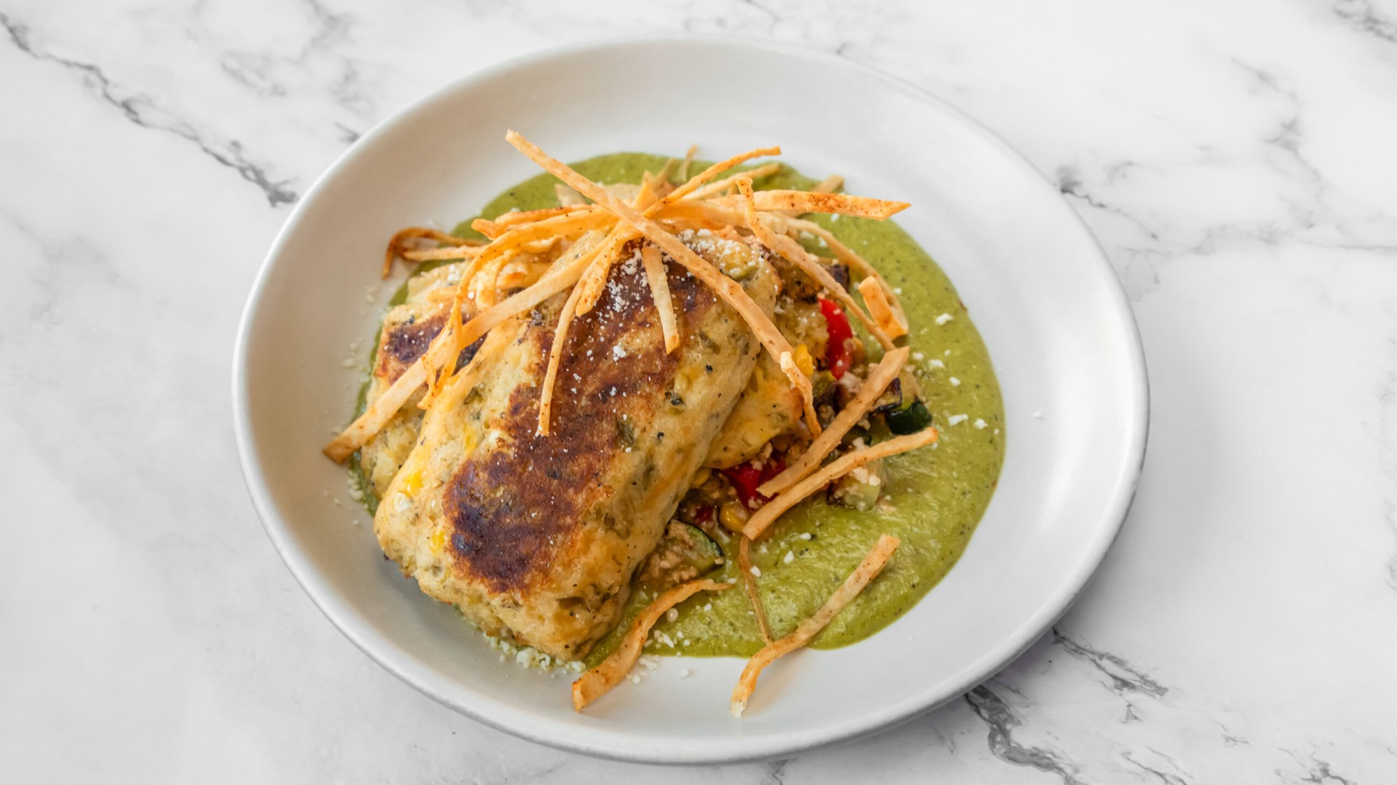 A plate of cooked chicken breast topped with fried strips, served on green sauce with vegetables.