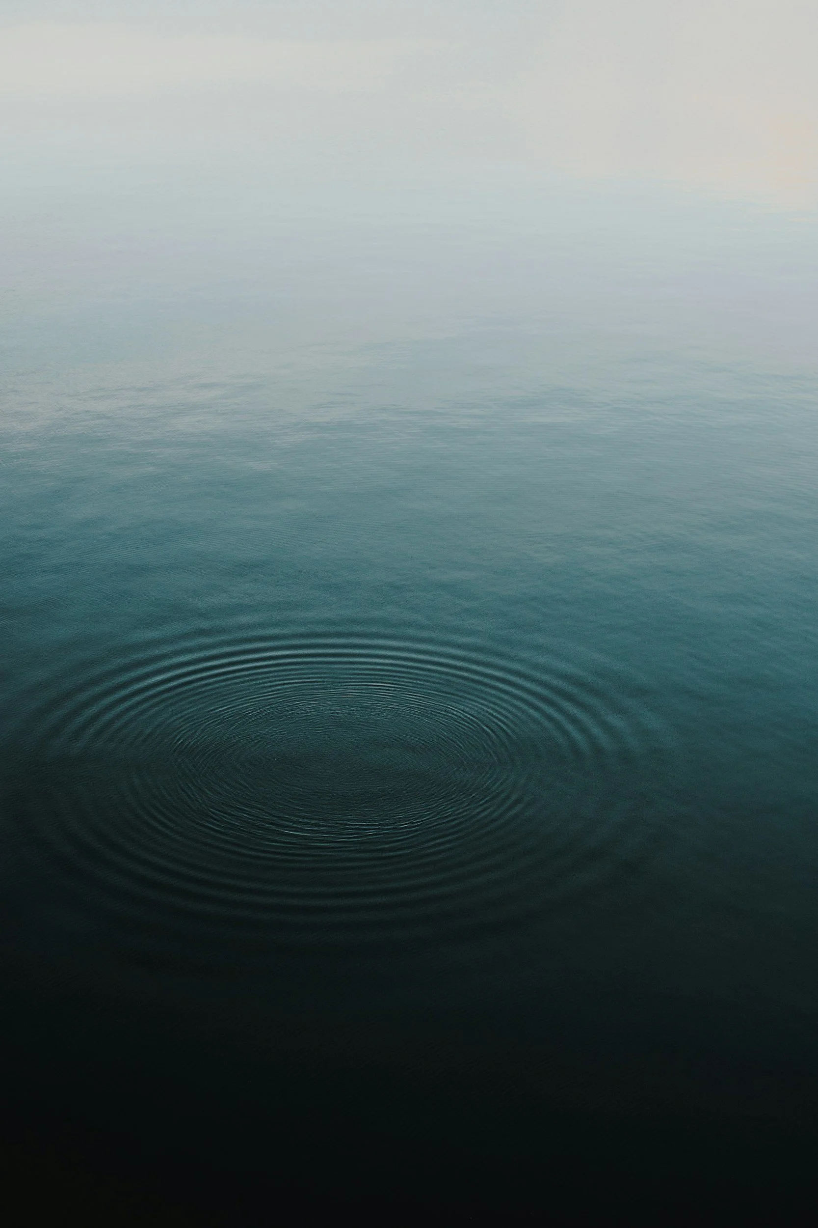 Calm ocean water with gentle ripples and a single water droplet causing ripples in the foreground.
