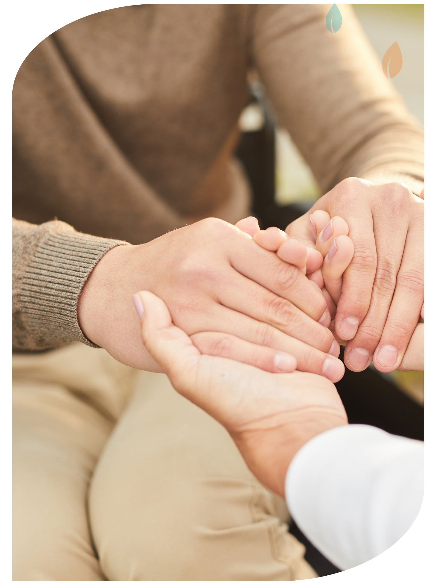 Close-up of two people holding hands, with one person wearing a brown sweater and another person in a white shirt and beige pants.