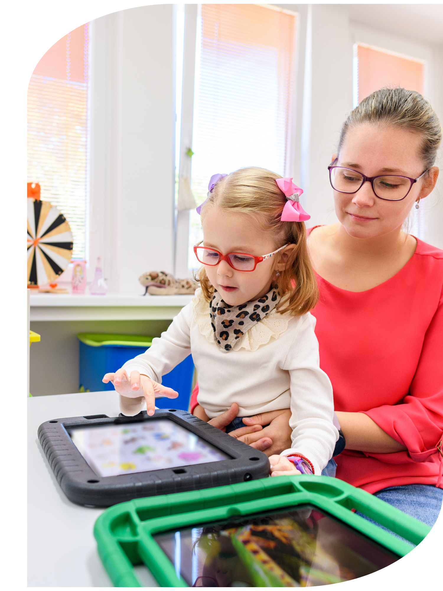 A woman and a young girl sitting at a table, using a tablet device while a health worker offers support.