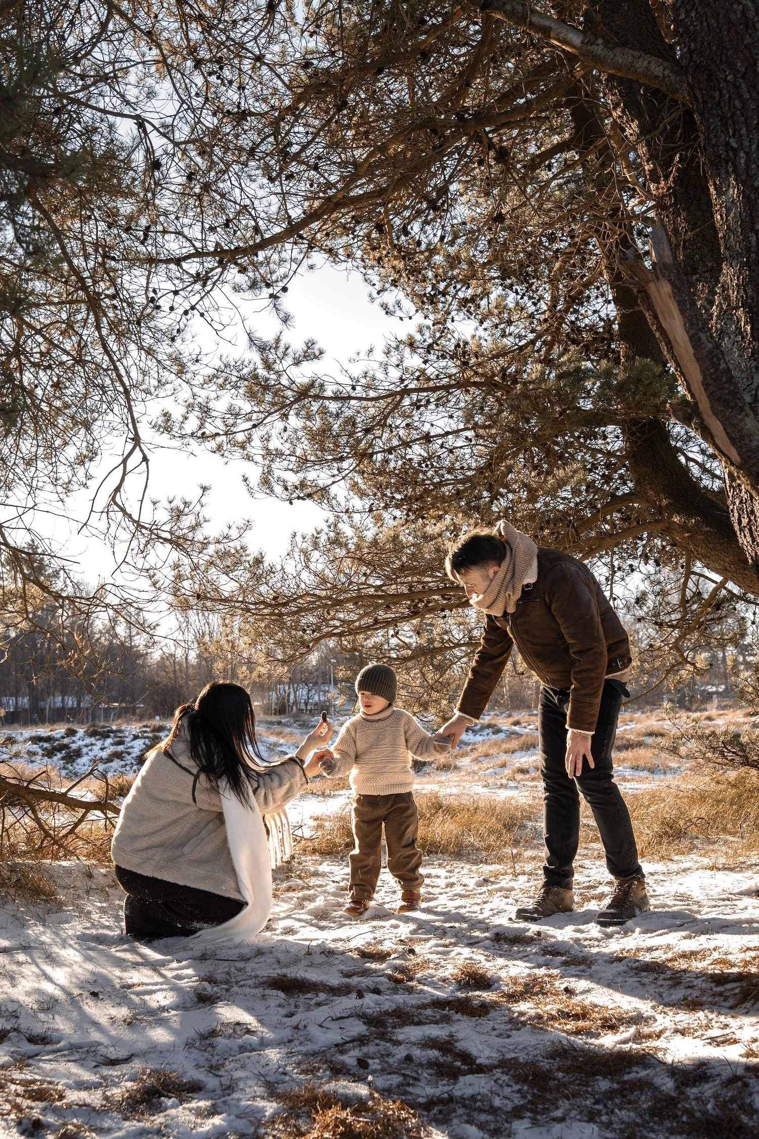 3 årig dreng og mor og far til familiefotografering i sneen og solen i naturområde i gilleleje i januar. De har beige striktøj på med brune nuancer