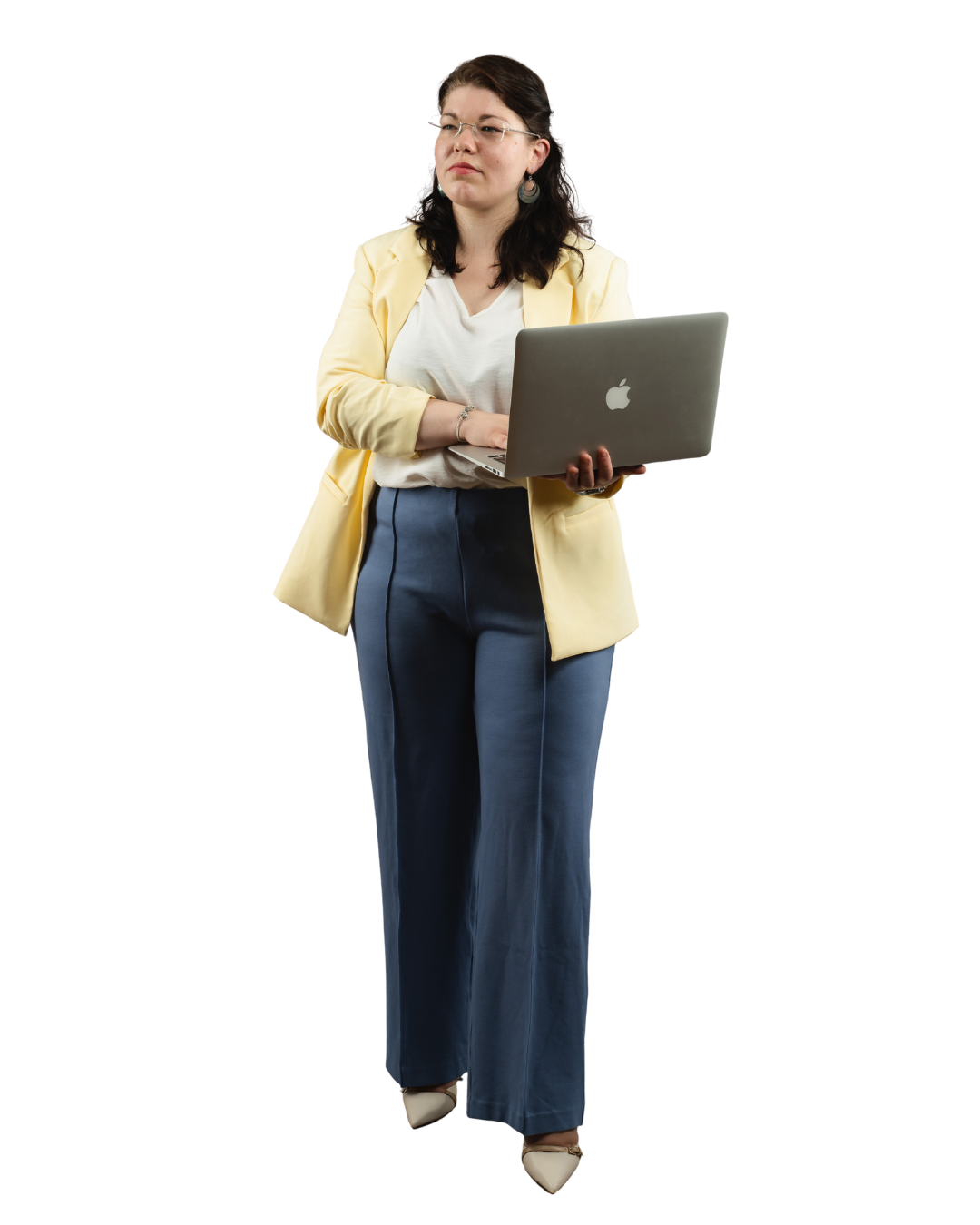 Eine Frau in einem gelben Blazer und blauer Stoffhose steht vor grauem Hintergrund und hält einen geöffneten Laptop.