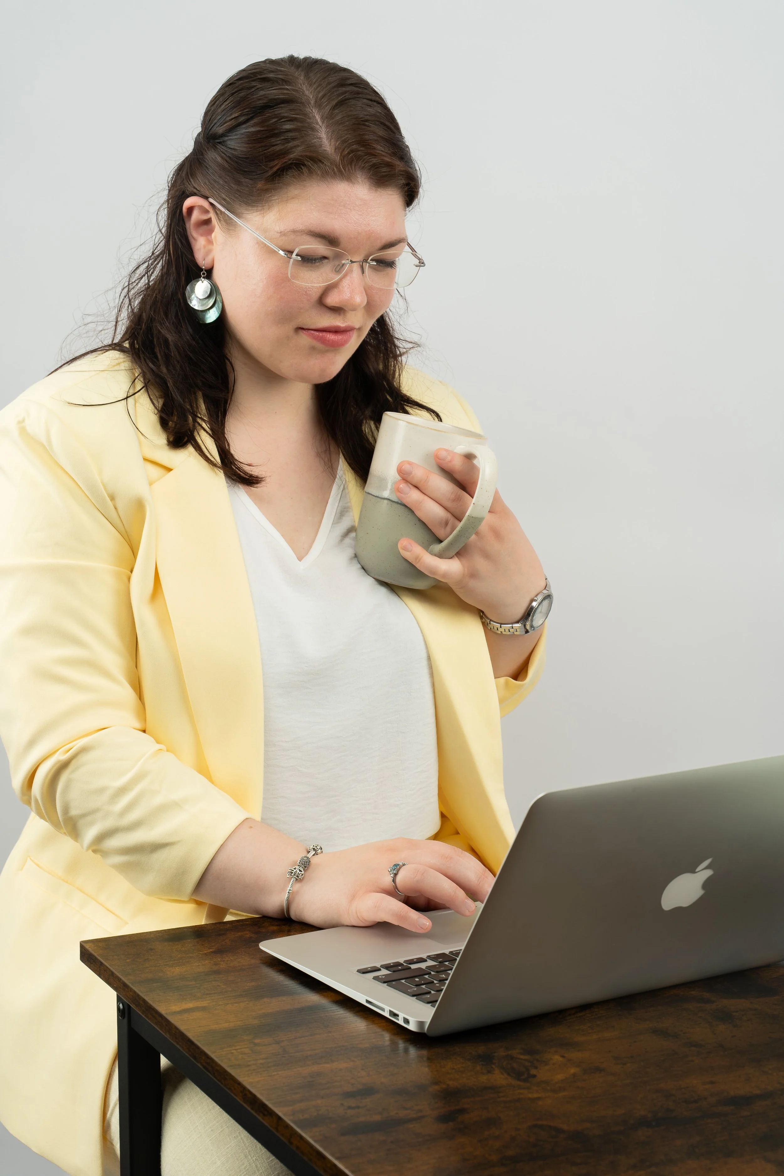 Seitenansicht einer Frau im hellgelben Business-Outfit, die am Laptop tippt. Die Szene wirkt fokussiert und professionell vor einem schlichten, hellgrauen Hintergrund.