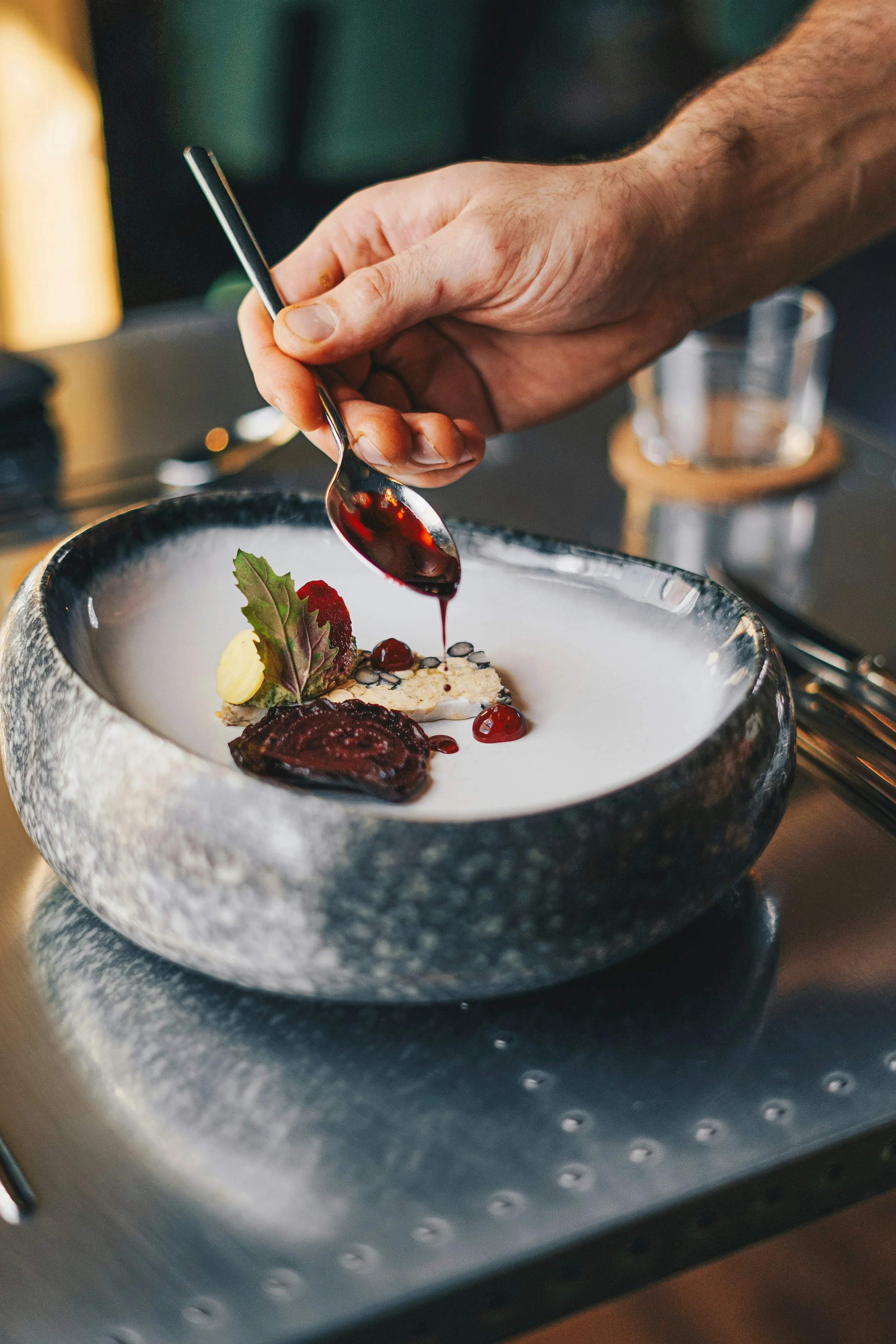 A chef drizzling sauce over a plated dessert with garnishes, on a black stone bowl. Michelin Star