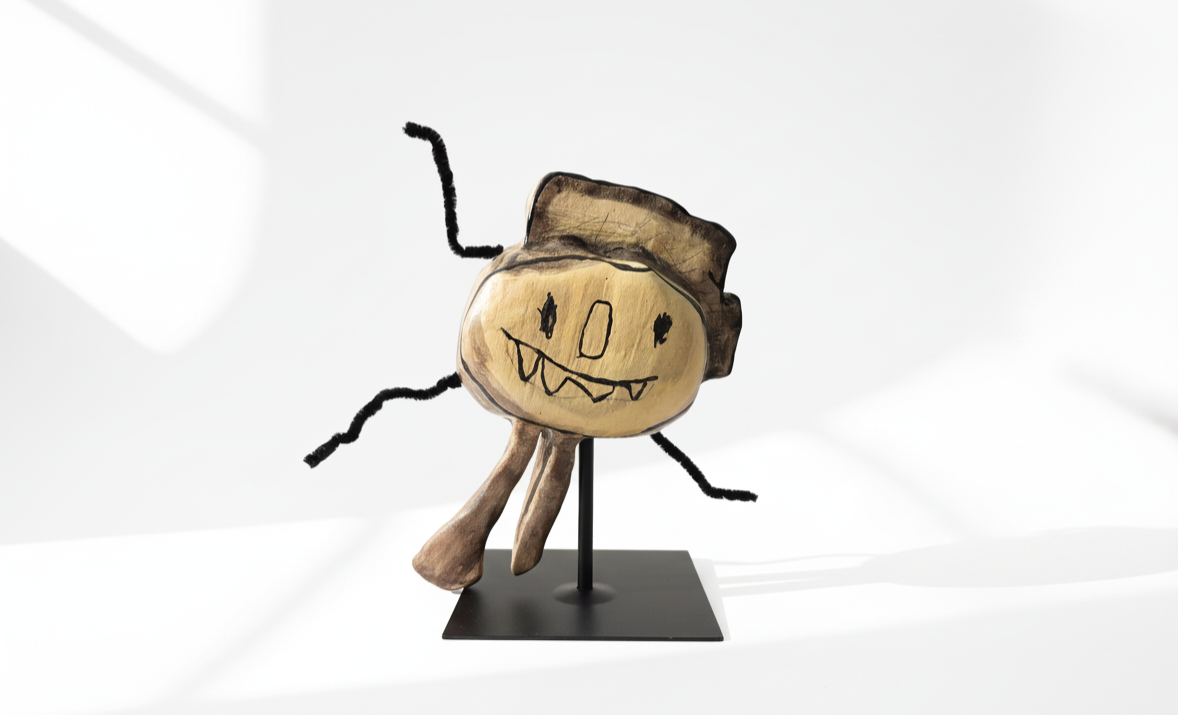 Wooden toy with a carved face, painted with a cartoonish smile, mounted on a black stand with drawn arms and a mischievous expression against a white background.