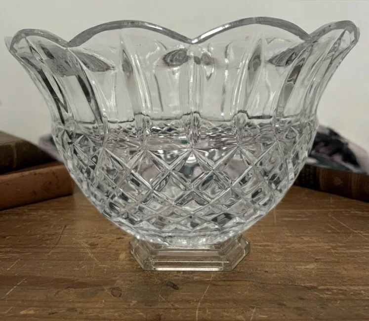 A clear glass decorative bowl with a diamond pattern and scalloped edges, placed on a wooden surface.