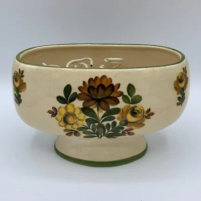 Cream-colored ceramic bowl with yellow and brown floral patterns and a green rim, resting on a white surface.