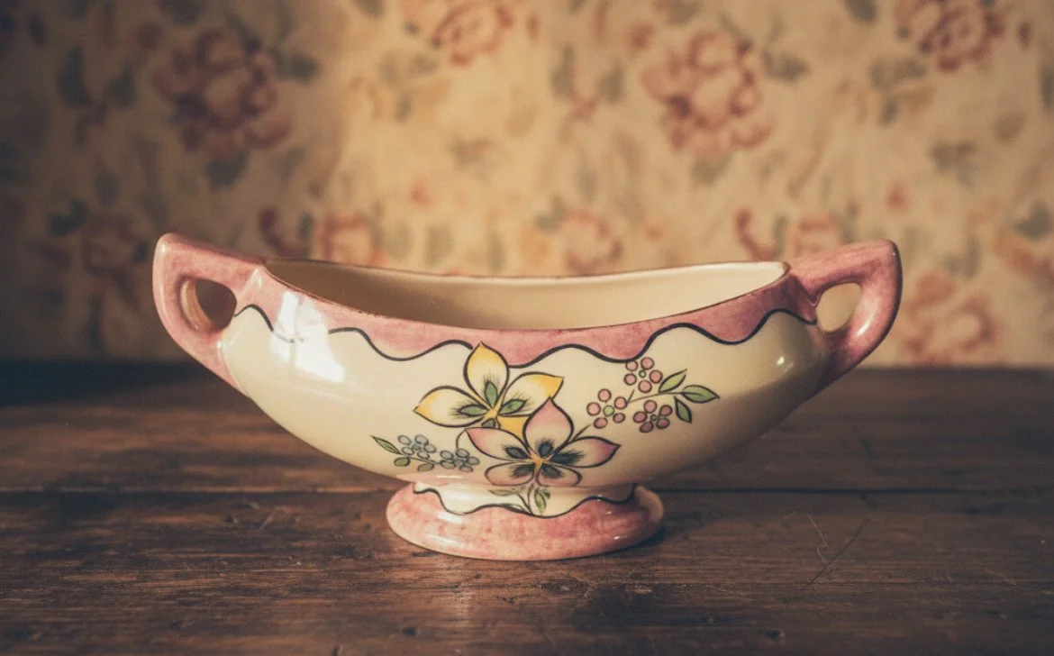 A decorative ceramic bowl with pink handles and floral design, placed on a wooden surface.