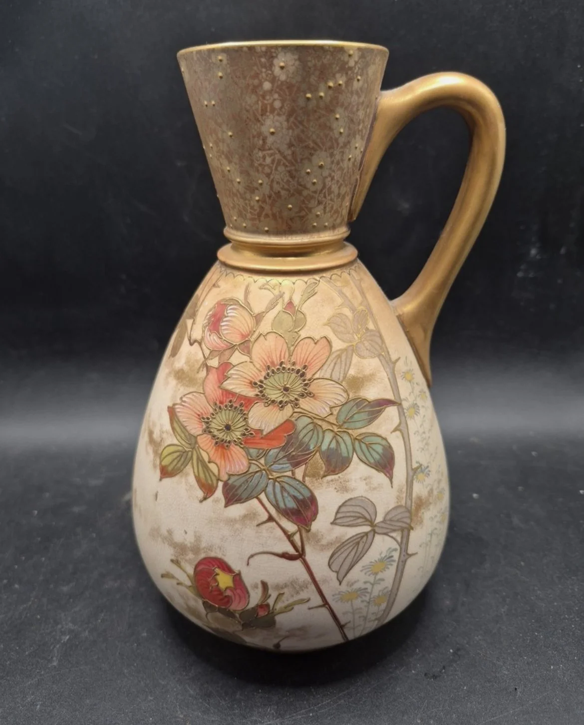 Decorative ceramic pitcher with floral and geometric patterns, featuring pink and green flower illustrations, gold accents, and a curved handle.
