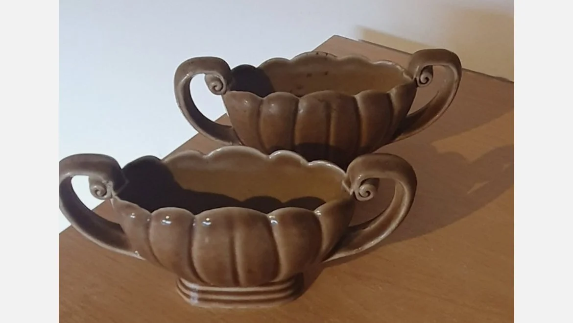Two brown ceramic teacups with carved circle patterns on a wooden surface.