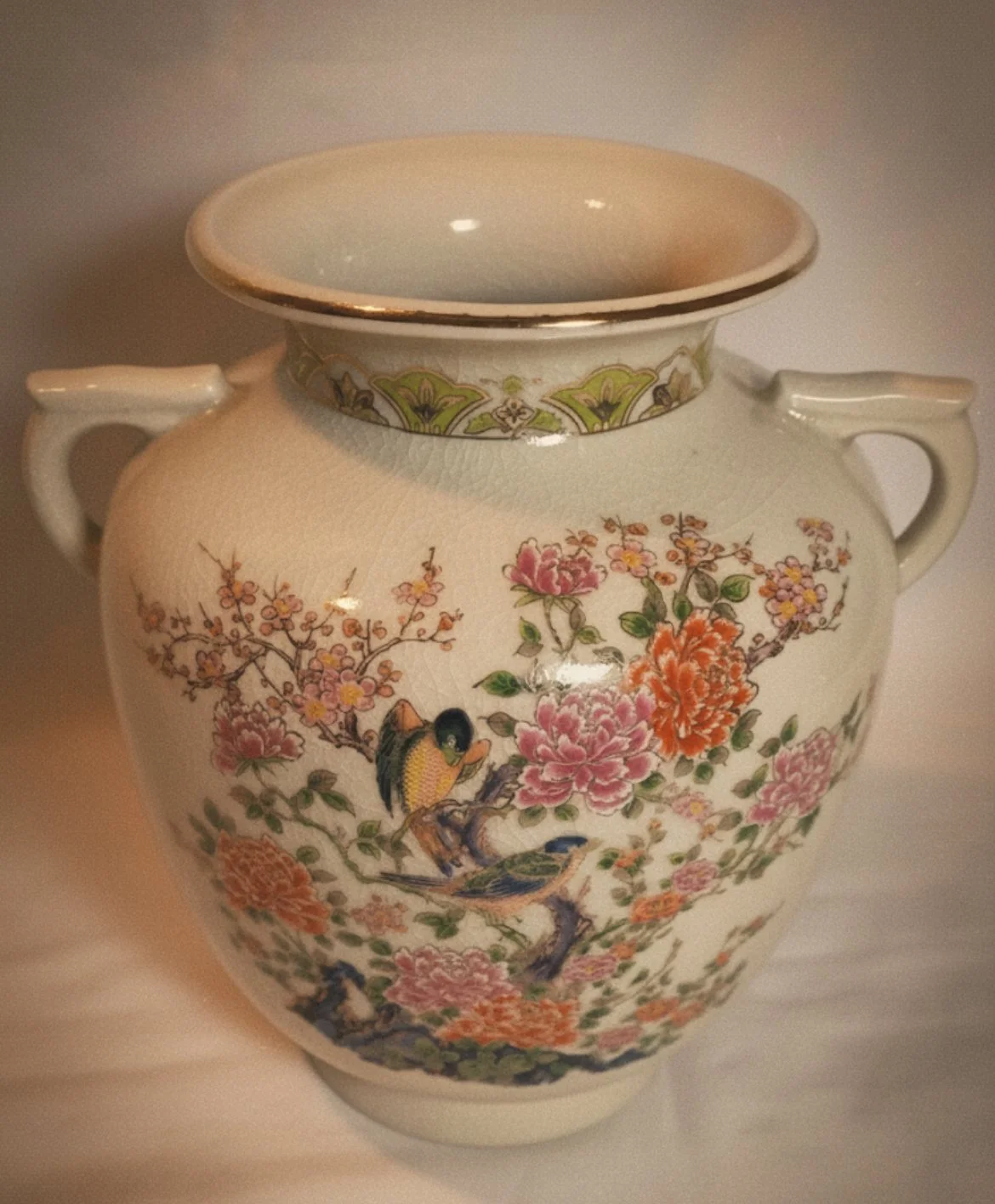 A decorative ceramic vase with floral and bird patterns, cream-colored background, gold accents, and two handles.