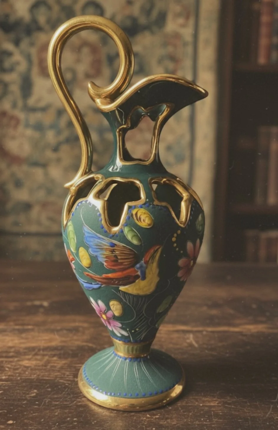 Decorative ceramic vase with gold accents, painted with a colorful bird and floral design, placed on a wooden surface.
