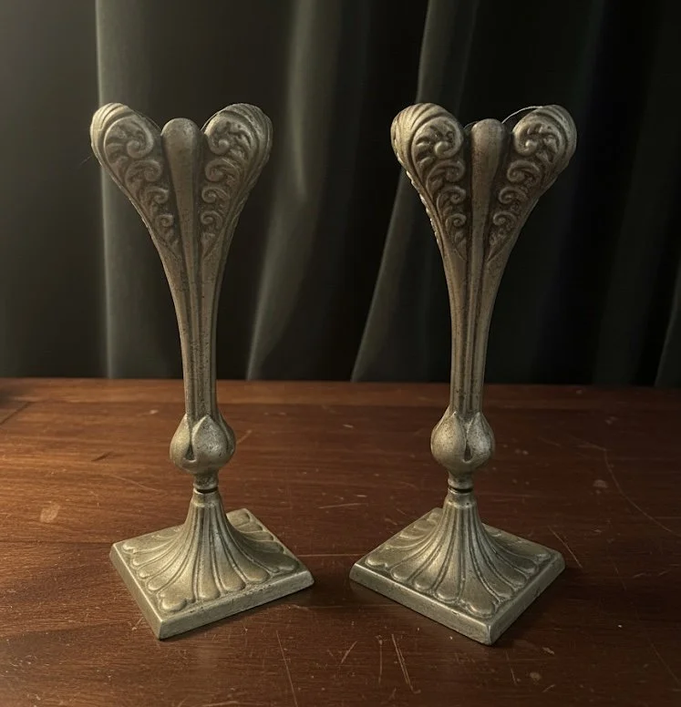 Two ornate, antique-style candle holders with carved decorative patterns on a wooden surface.