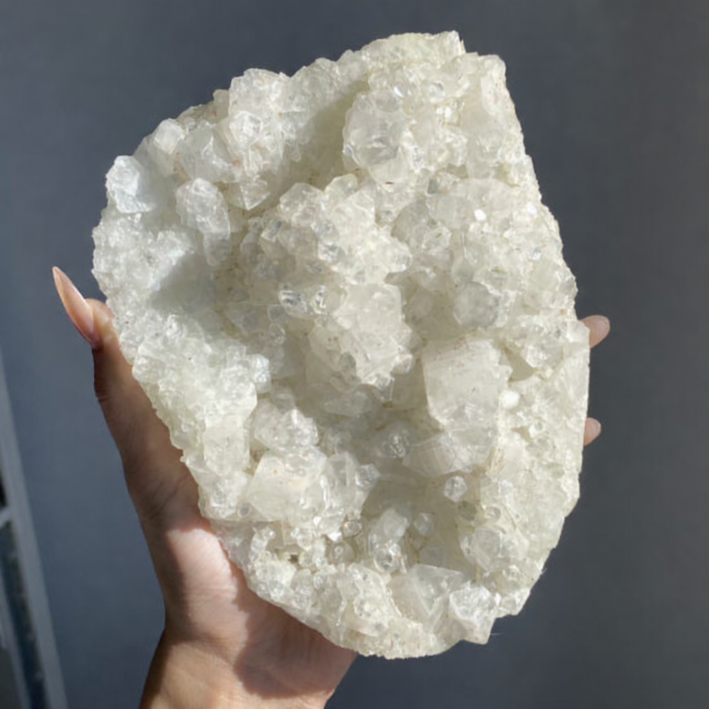 A hand holding a large, white crystalline mineral specimen with a rough, irregular shape and multiple sparkling crystal points.