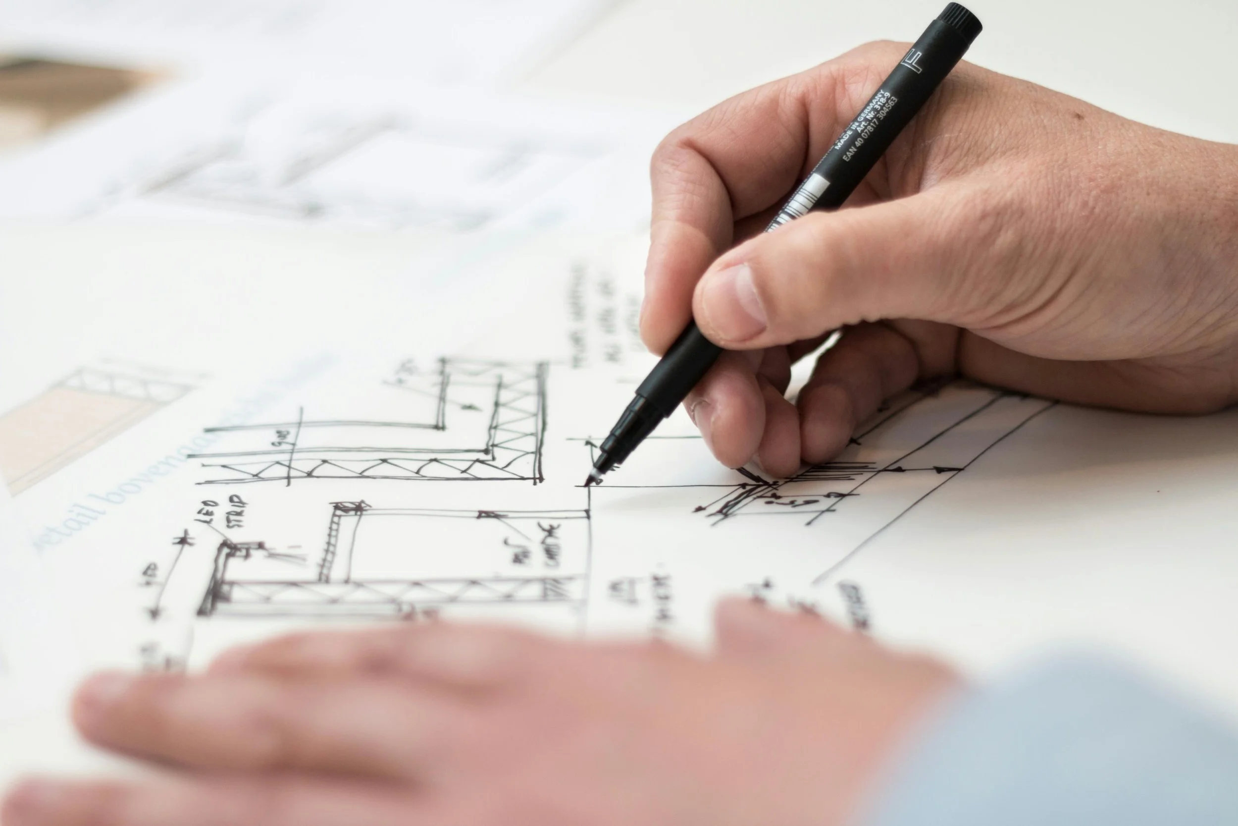 A person drawing a construction plan with a black marker on white paper, showing technical sketches of a building structure.