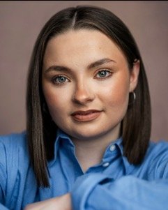 A woman with straight dark hair and blue eyes, wearing a blue shirt, looking into the camera with a slight smile.