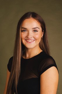 A young woman with long brown hair, smiling, wearing a black top, against a green background.