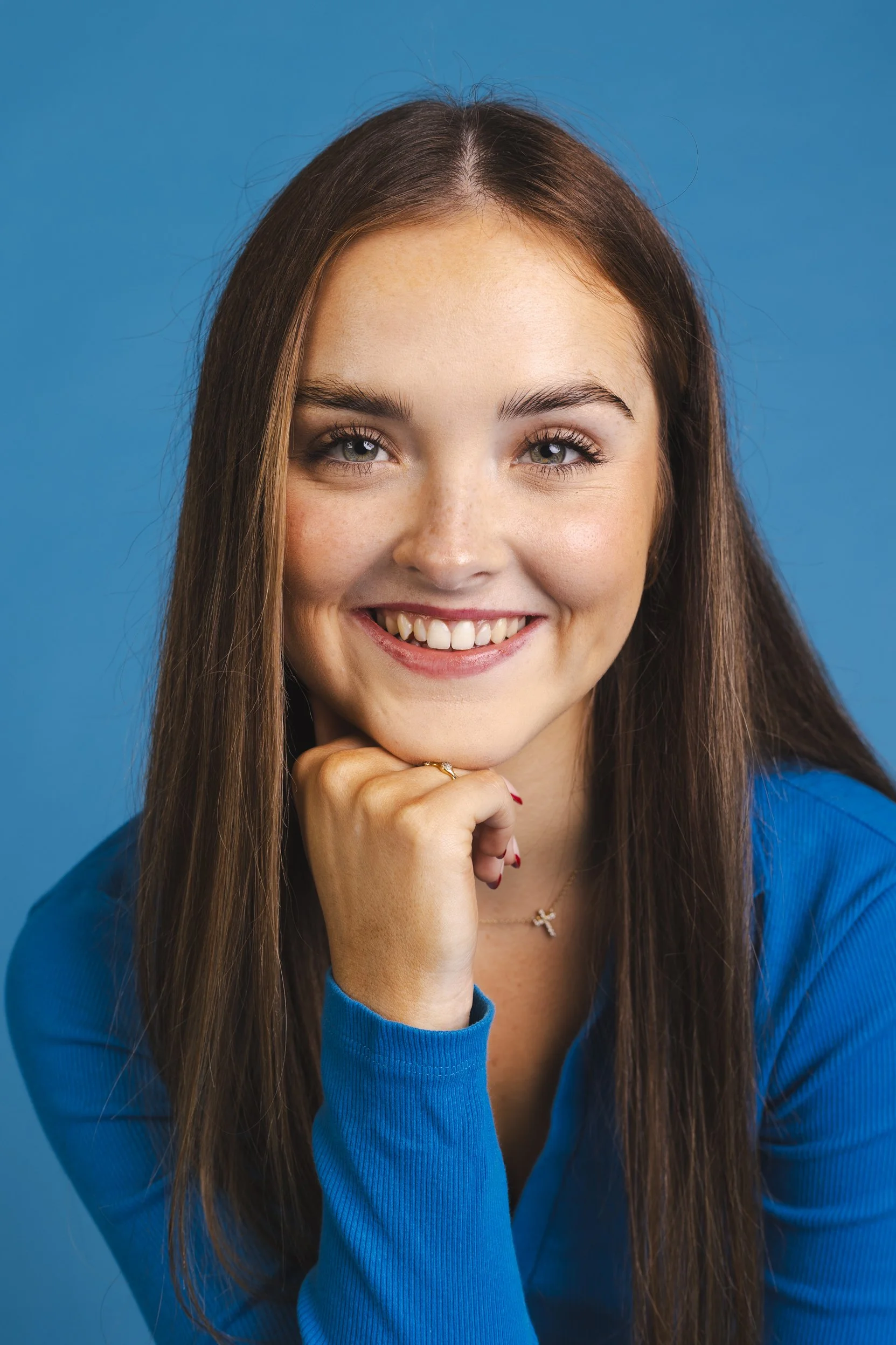 A young woman with long brown hair, smiling, wearing a black top, against a green background.