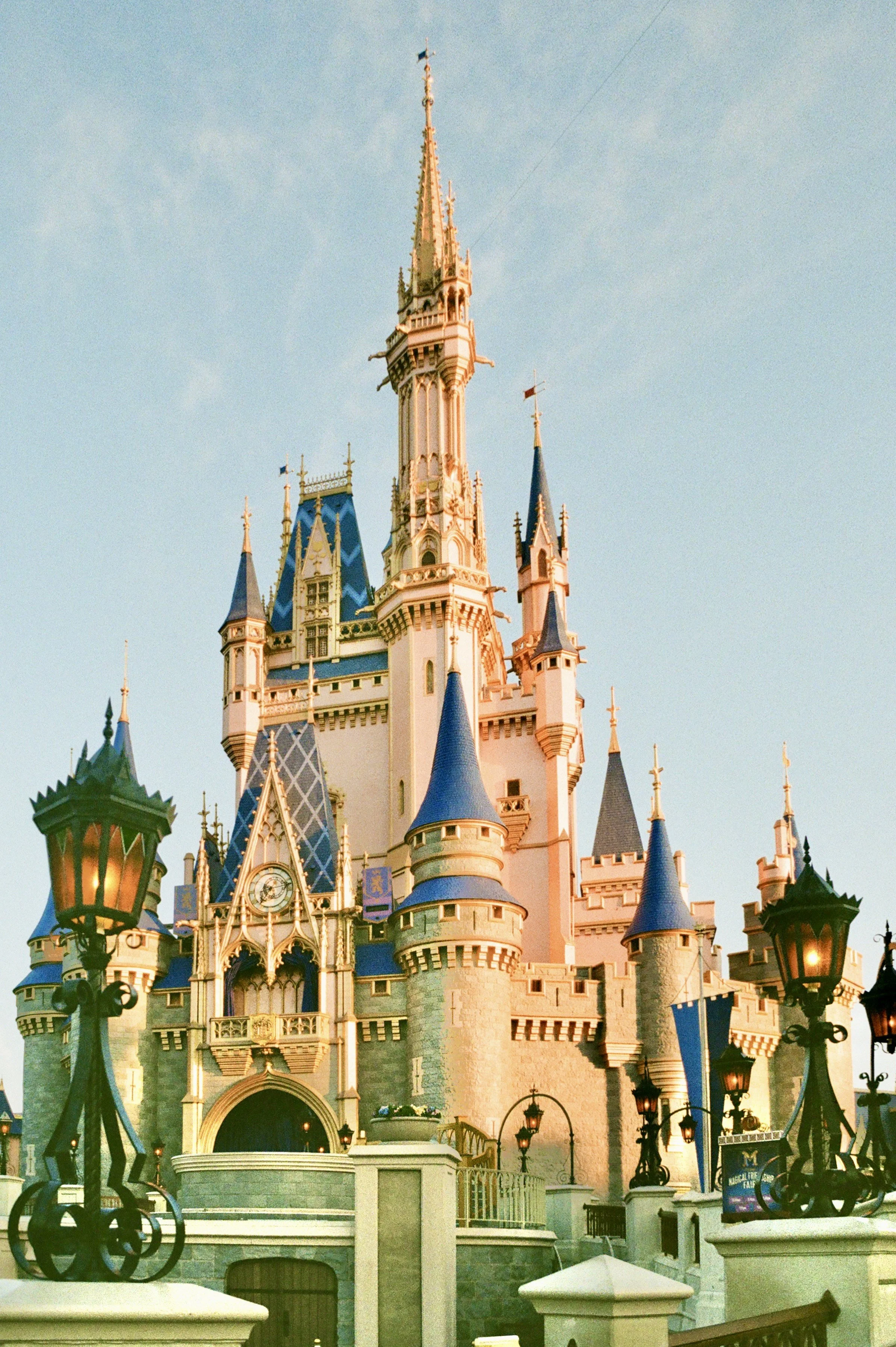 A colorful castle with pink walls and blue rooftops, topped with spires, at a Disney theme park during daytime.