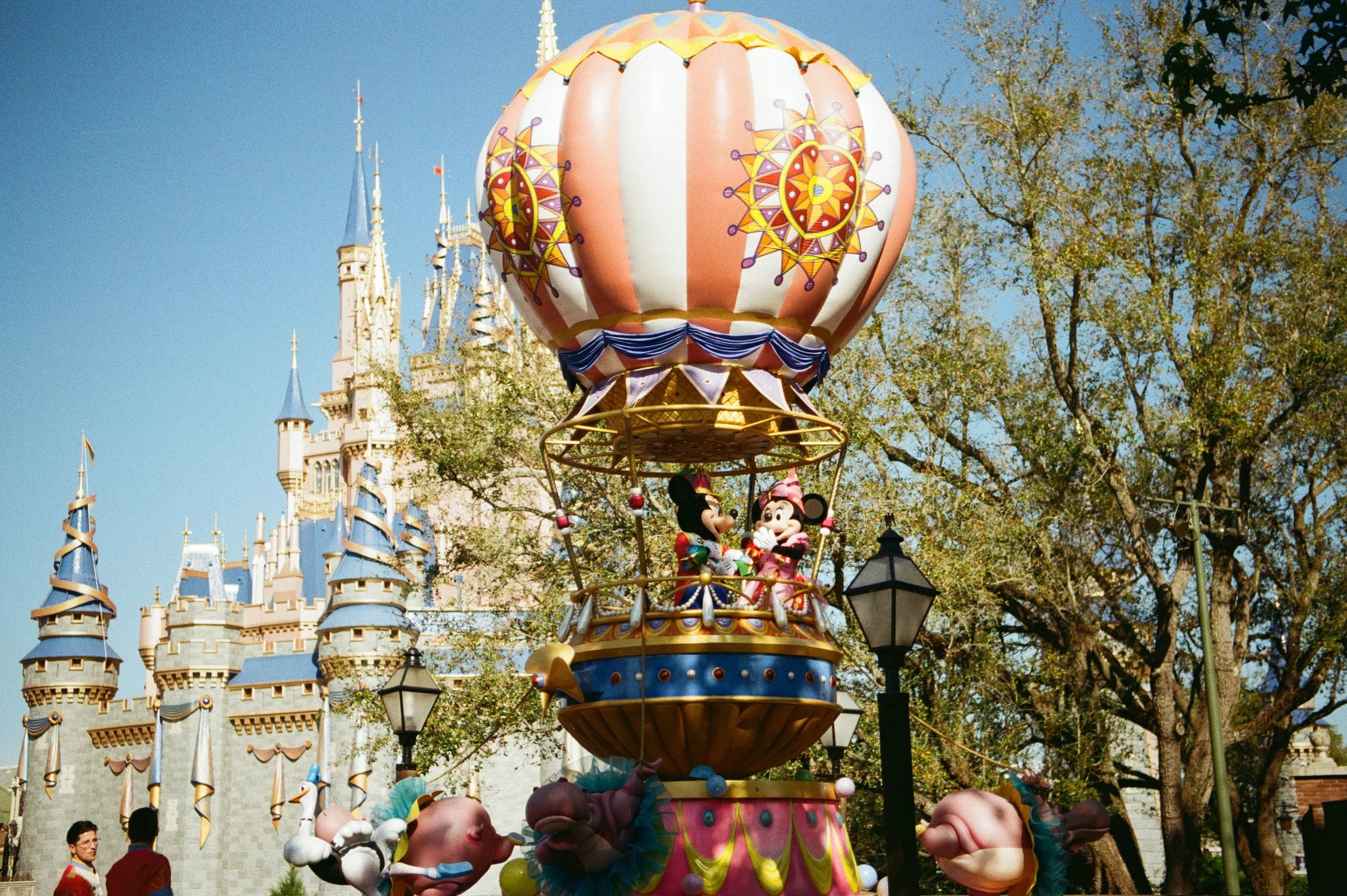 Disneyland parade float featuring Mickey Mouse and Minnie Mouse in a hot air balloon with a castle in the background.