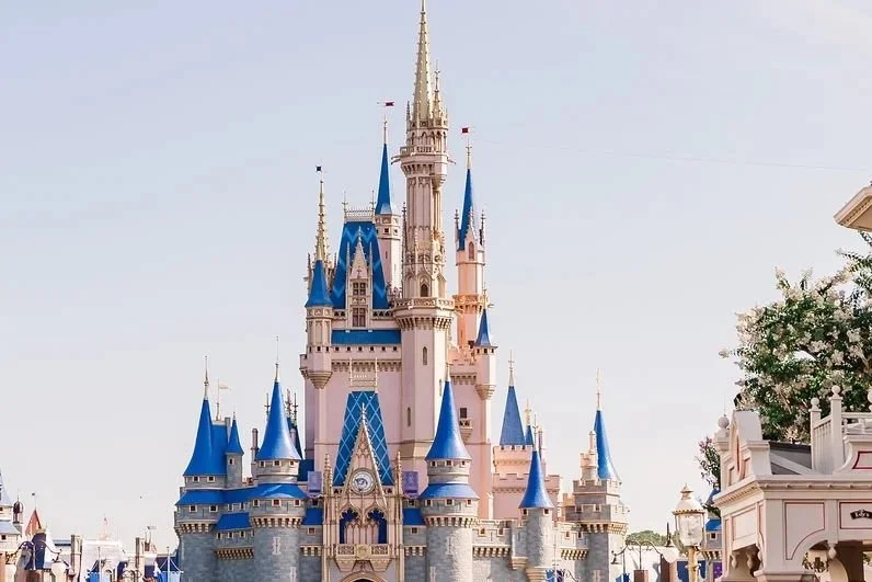Colorful Disney castle with tall spires and banners, set against a clear sky.
