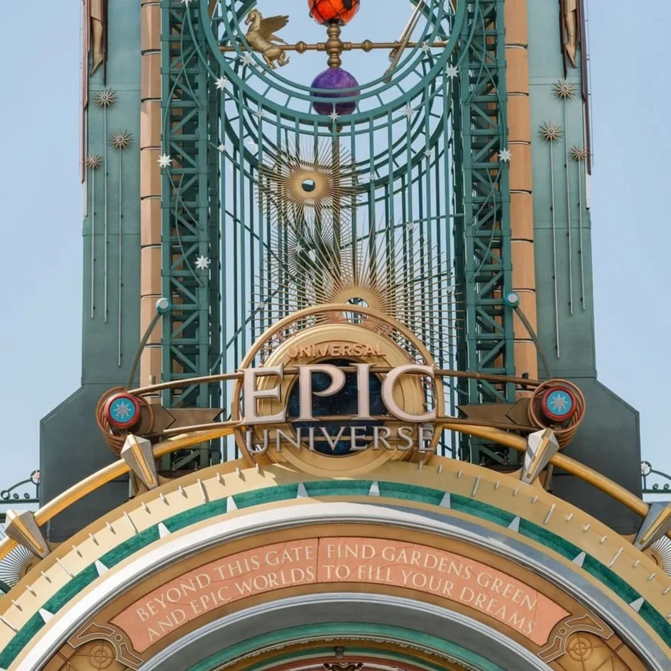 Close-up of the entrance sign to Universal Epic Universe theme park with decorative celestial and clock elements above the logo and a quote about finding gardens beyond the gate.