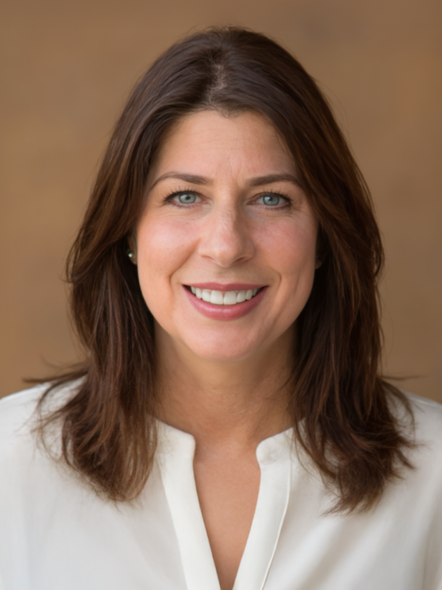 A woman with brown collar-bone length hair with blue eyes, wearing a white shirt.