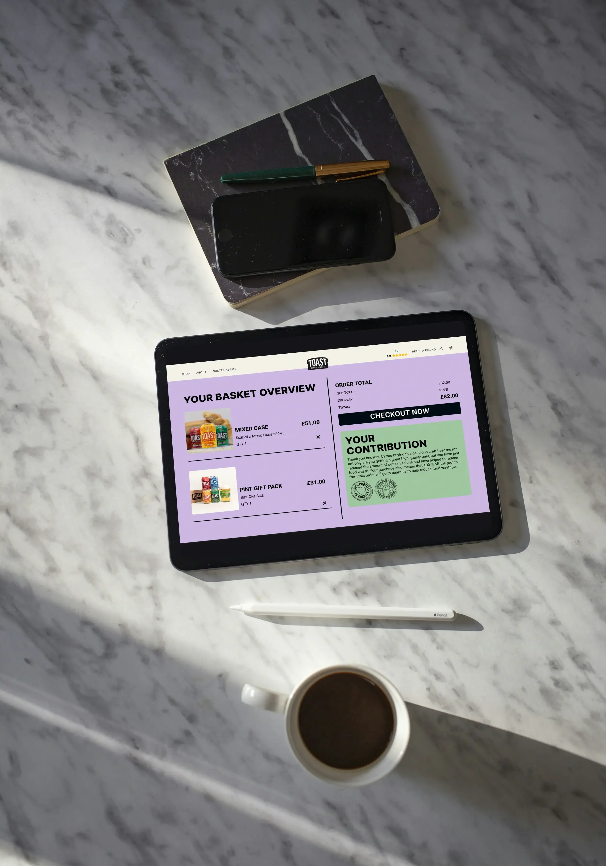 A workspace with a marble surface holding a tablet displaying an online shopping basket for a craft beer delivery service, a white pen, a coffee mug filled with coffee, a smartphone, a black pen, and a small marble-topped table with no items.