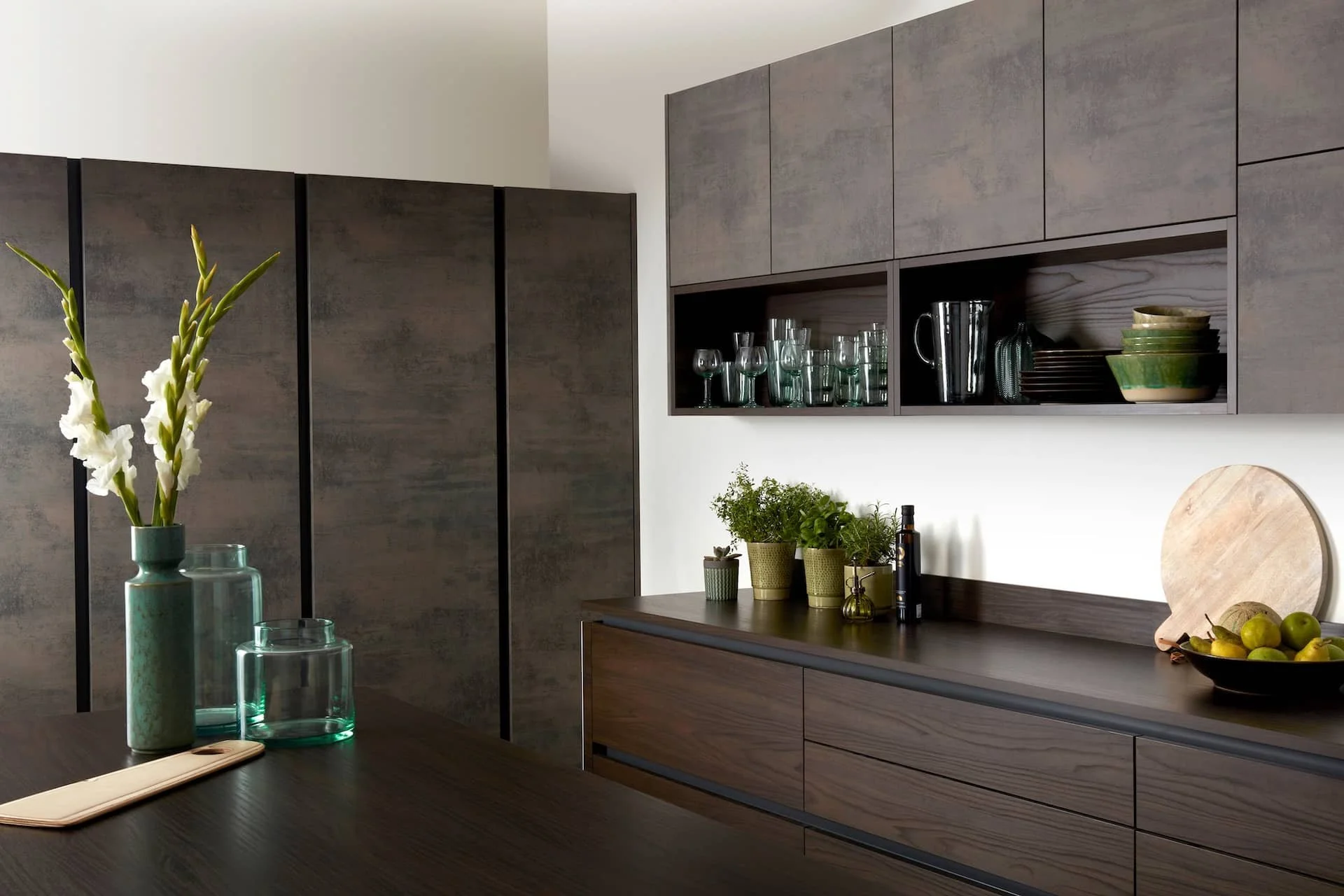 Modern kitchen with dark wood cabinets, glassware, and decorative plants.