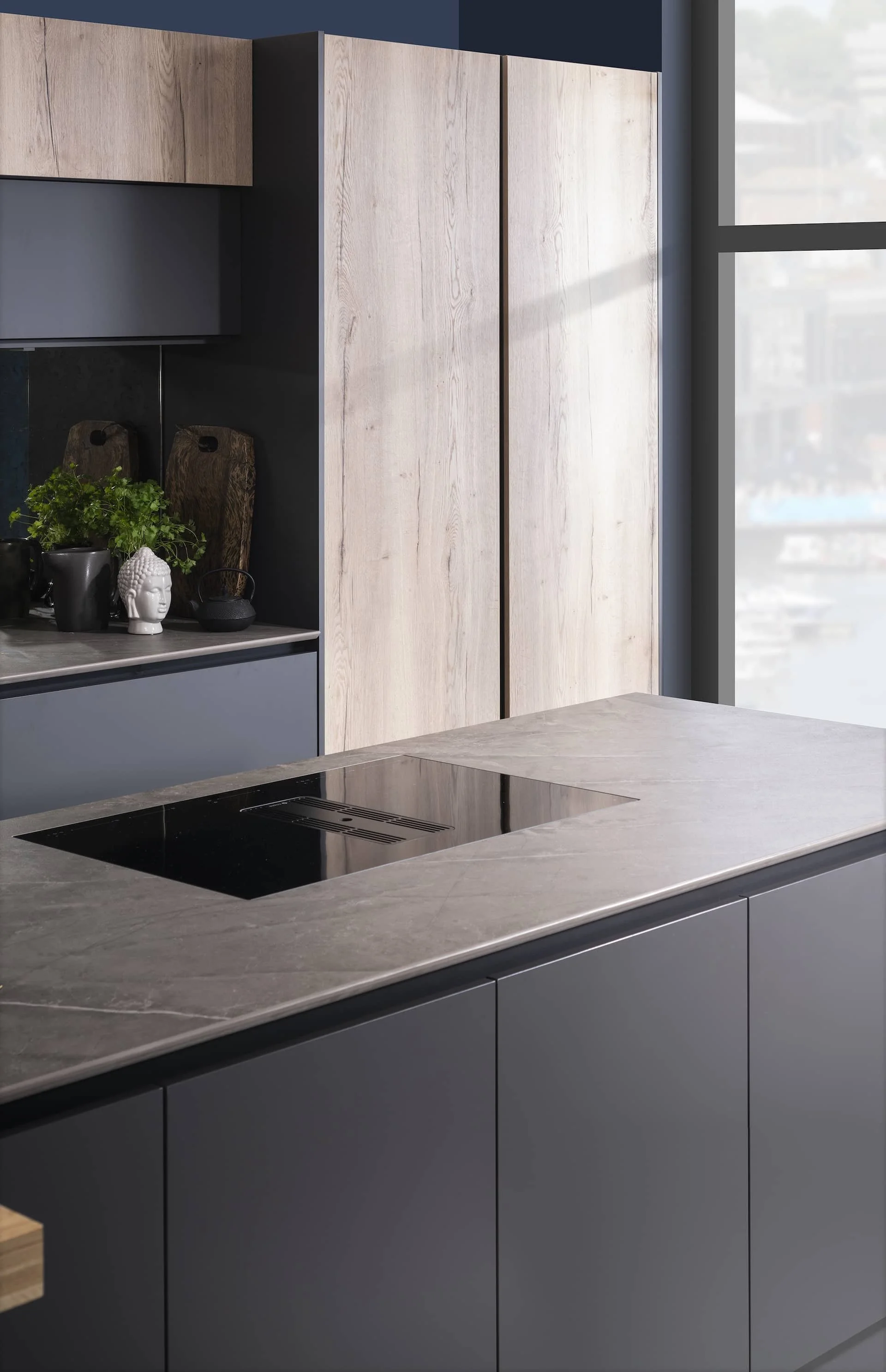 Modern kitchen with dark gray cabinets, a marble countertop, and wooden cabinets under a large window.
