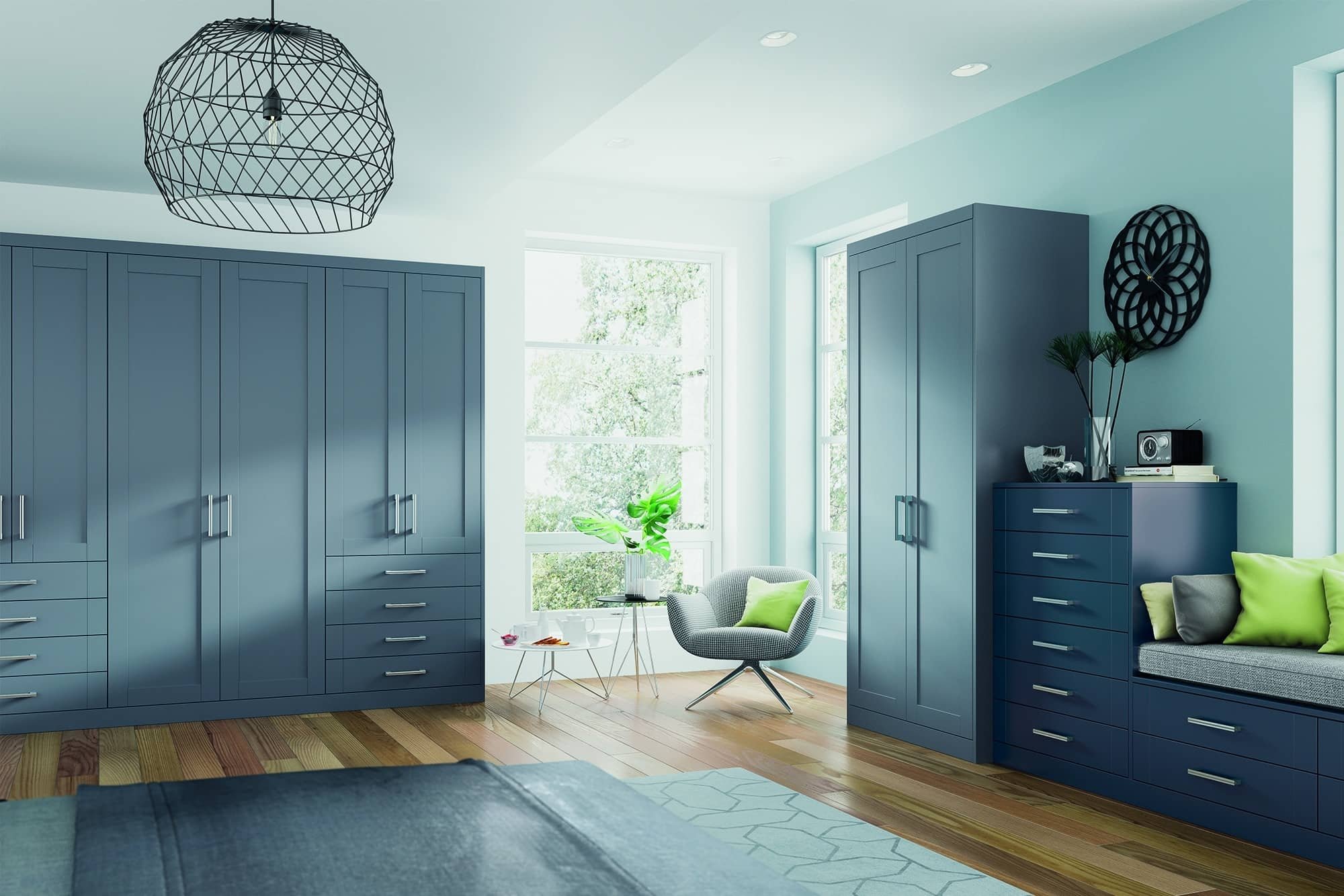 Modern living room with blue cabinets, a white armchair with a green pillow, a small side table with tea cups, large windows with trees outside, and a geometric black pendant light.