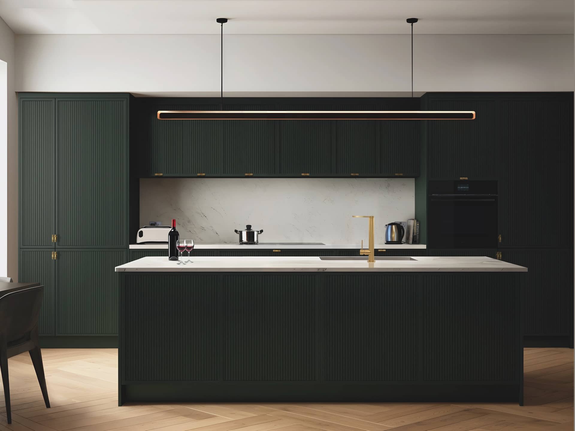 Modern kitchen with dark green cabinets, white marble backsplash, and a white marble kitchen island with a gold faucet. Items on the countertop include a wine bottle, two wine glasses, a toaster, a kettle, and a stove. A linear pendant light hangs ab
