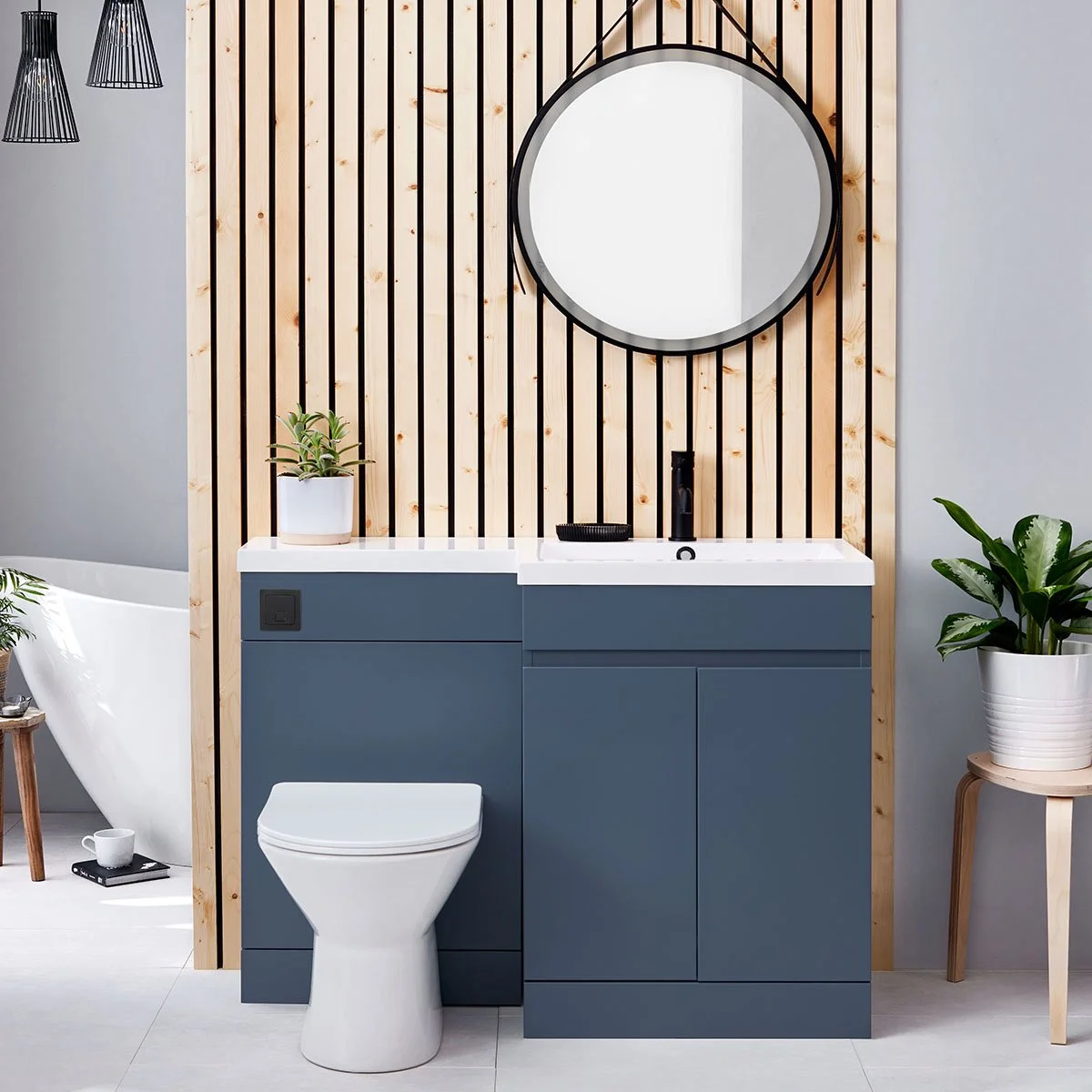 Modern bathroom with a wooden slat accent wall, a round mirror, blue vanity, white sink, potted plants, and decorative pendant lights.
