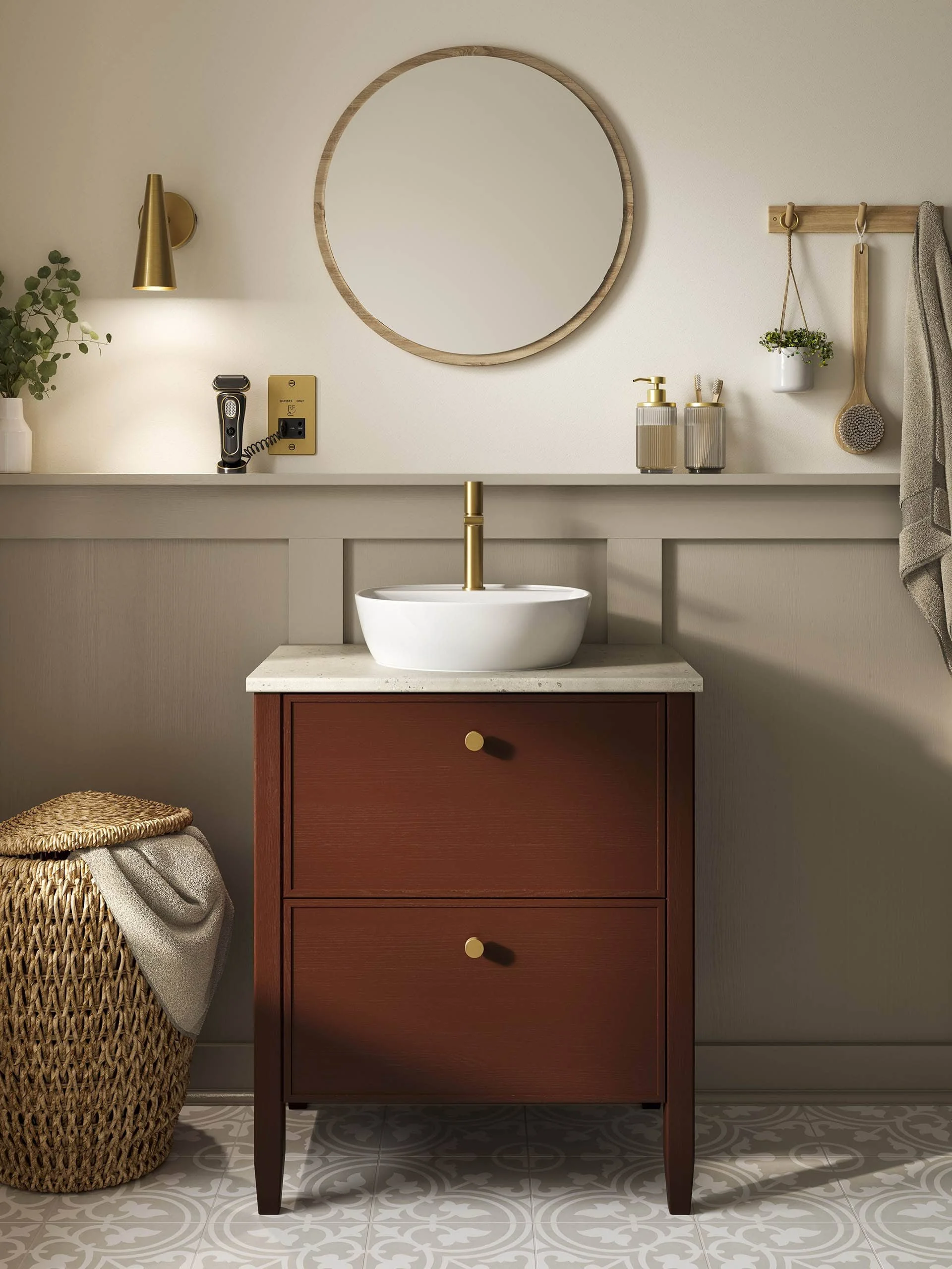 A bathroom with a wooden vanity, white sink with gold faucet, oval mirror, decorative wall light, wall-mounted plant, wooden hanging hooks with a cloth and bath brush, and a wicker basket with a towel.