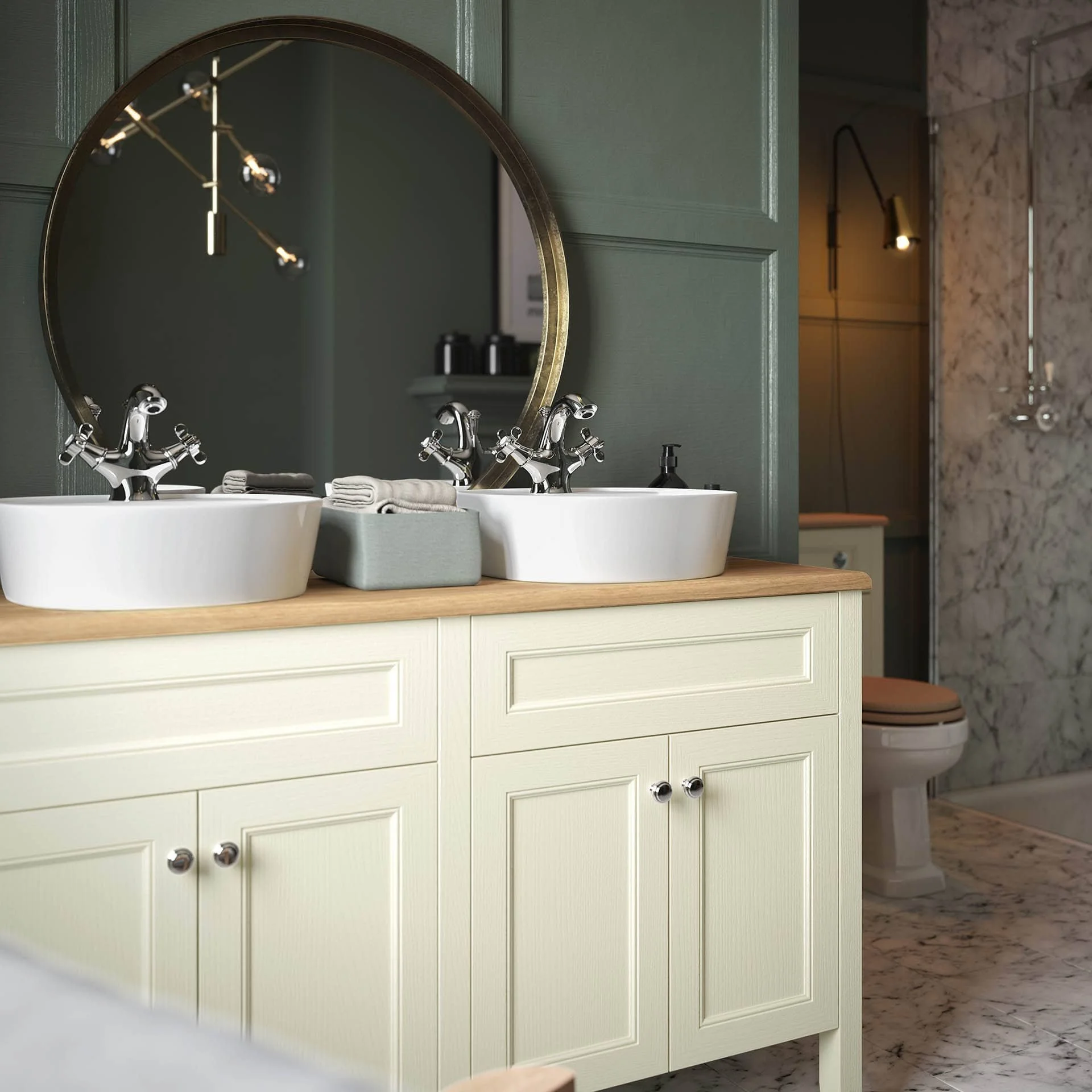 A bathroom vanity with two white vessel sinks, a round mirror with a gold frame, and a wooden countertop. There are two chrome faucets and a gray tray with towels. In the background, a marble shower area and toilet are visible.