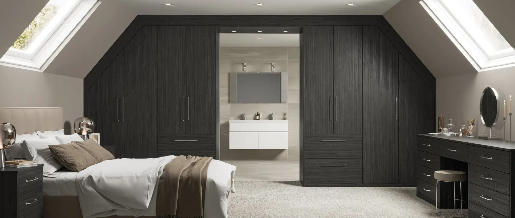 A modern bedroom with sloped ceilings and skylights, featuring a large bed with white bedding and brown pillows, black furniture including nightstands and a dresser, and an open doorway leading to a bathroom with a white vanity and a wall-mounted mir