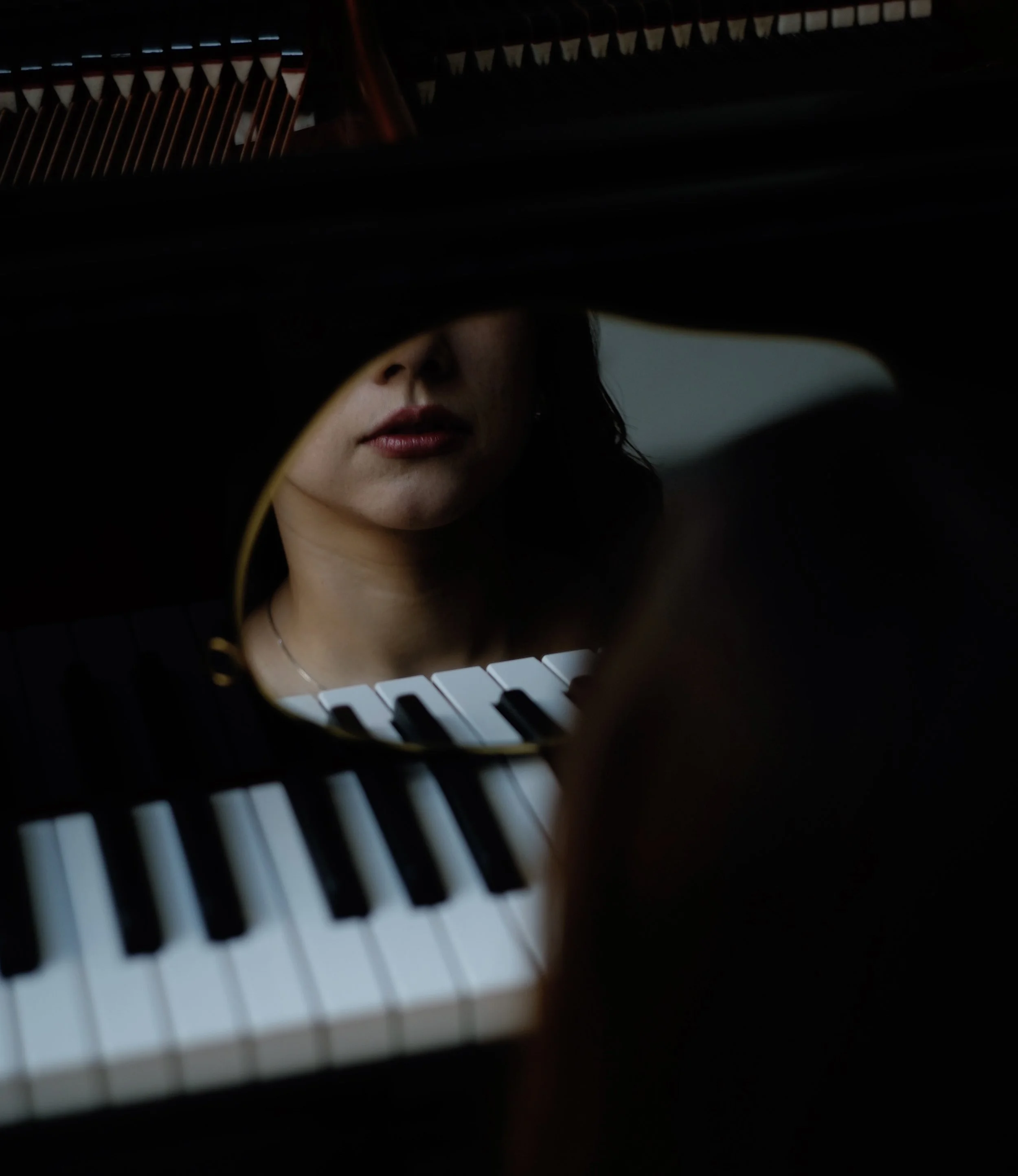 A woman's face is seen in a mirror reflection above the piano keys, with her lips visible and nose partially obscured.