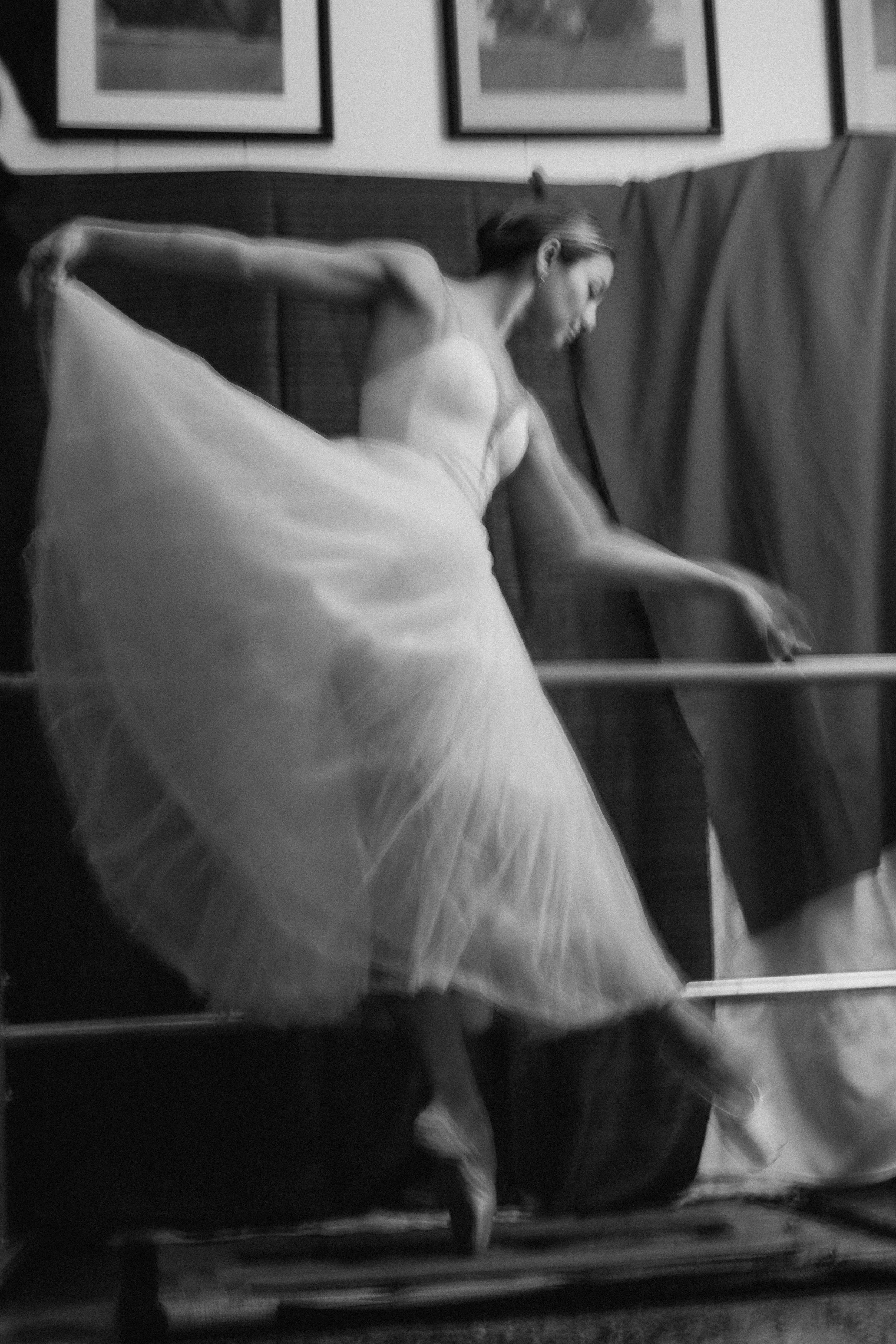 A woman in a ballet tutu and pointe shoes practicing dance at a barre in a studio.