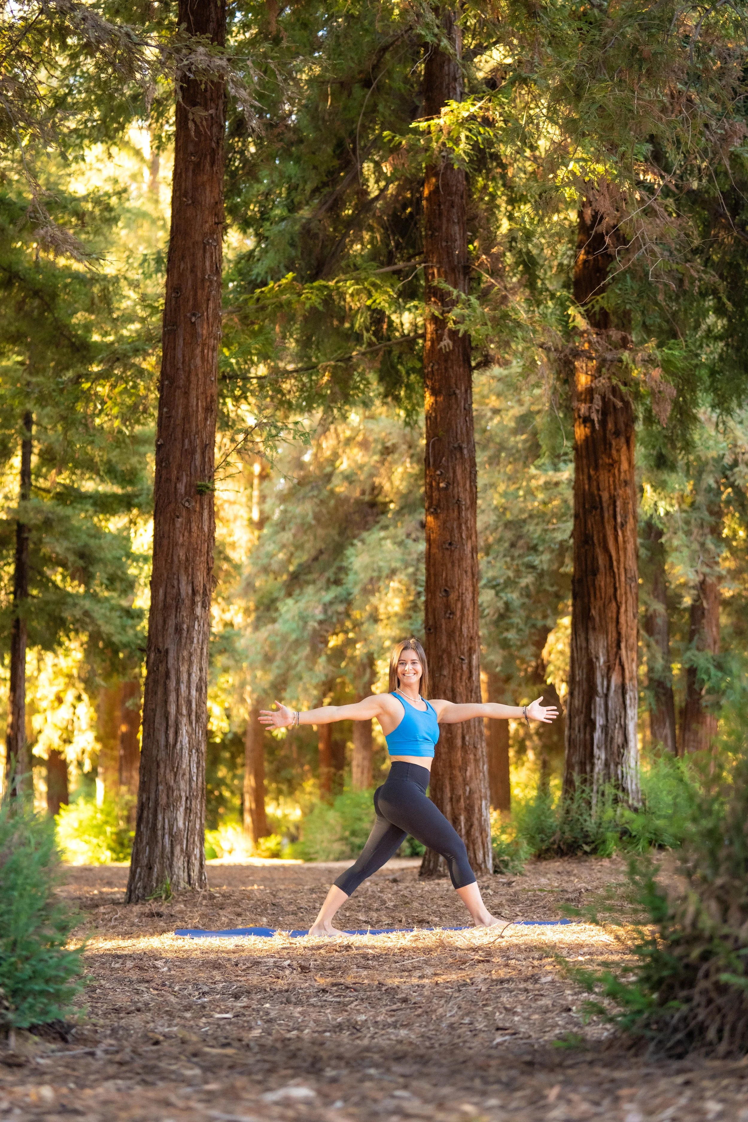 A woman practicing yoga outdoors in a forest during sunrise.