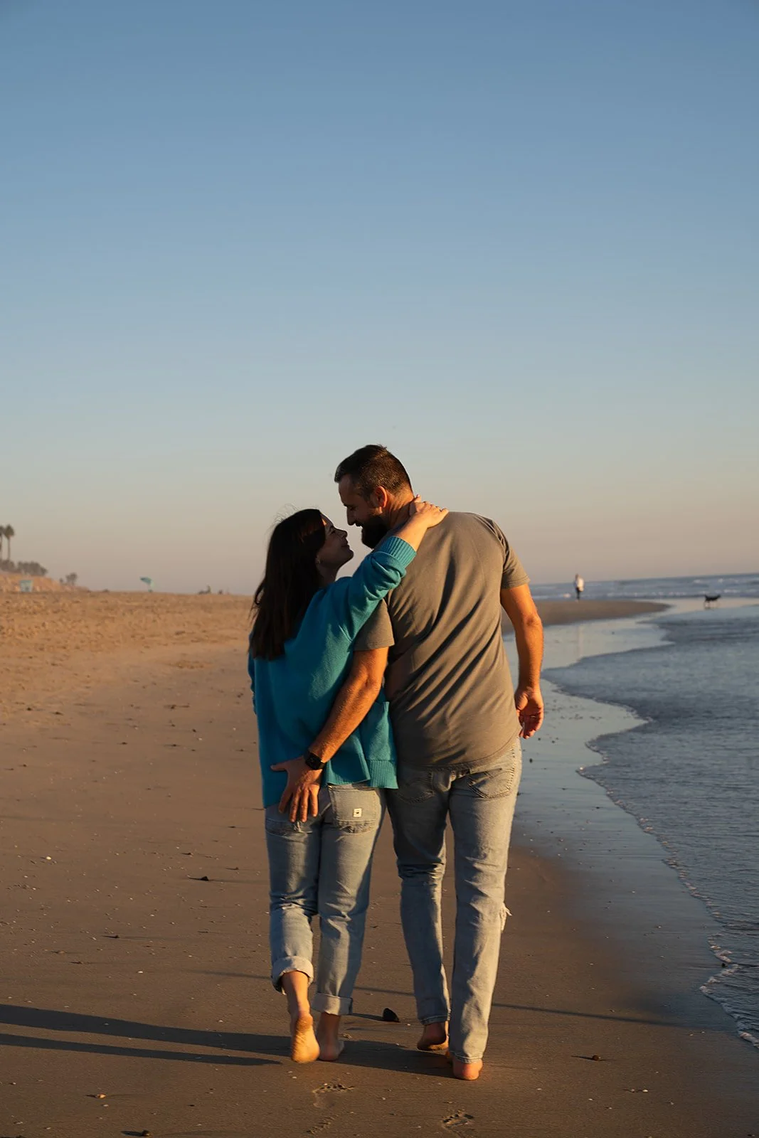A couple walking on the beach at sunset, embracing each other lovingly.