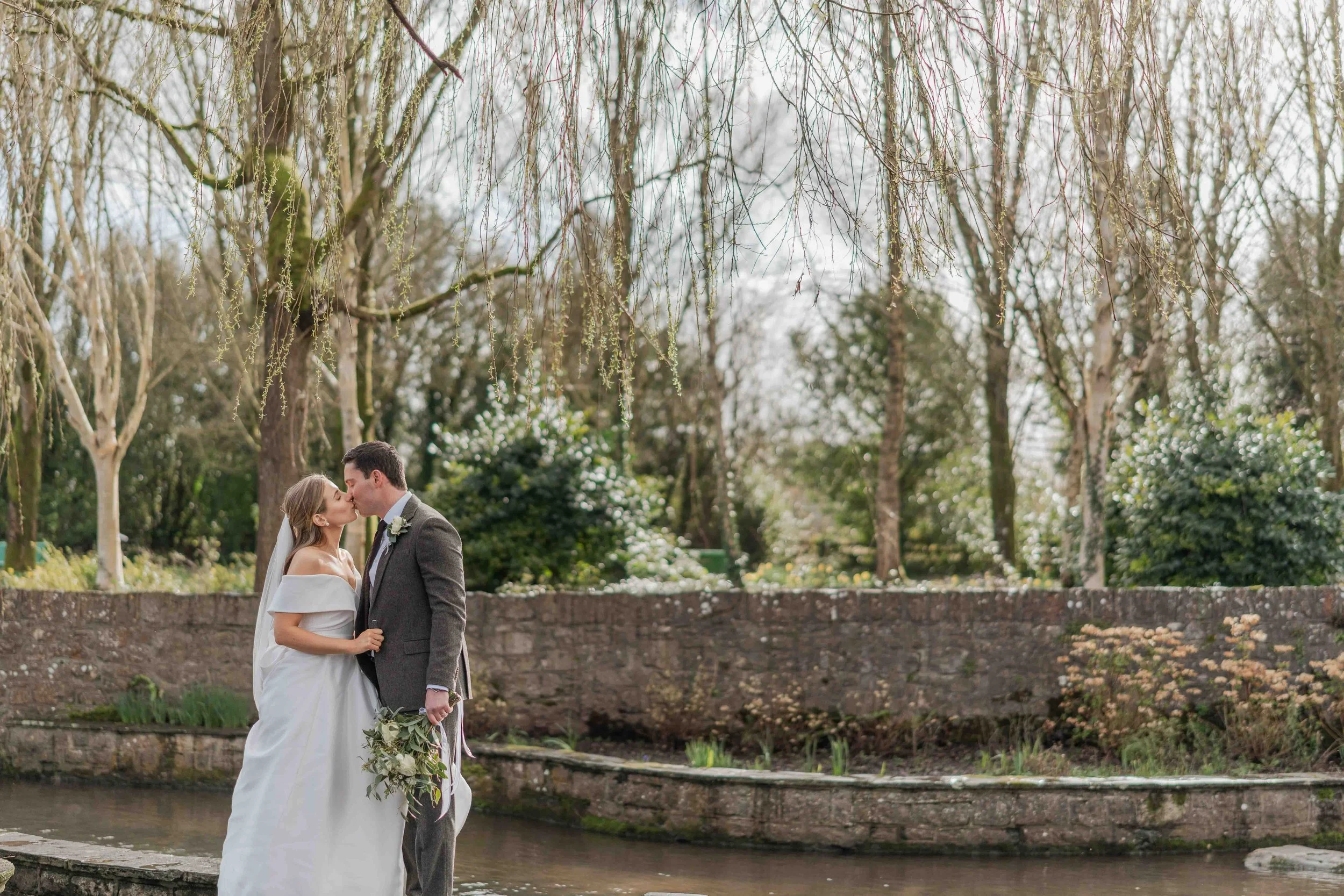 A bride and groom kissing beside a small stream in a garden during their wedding