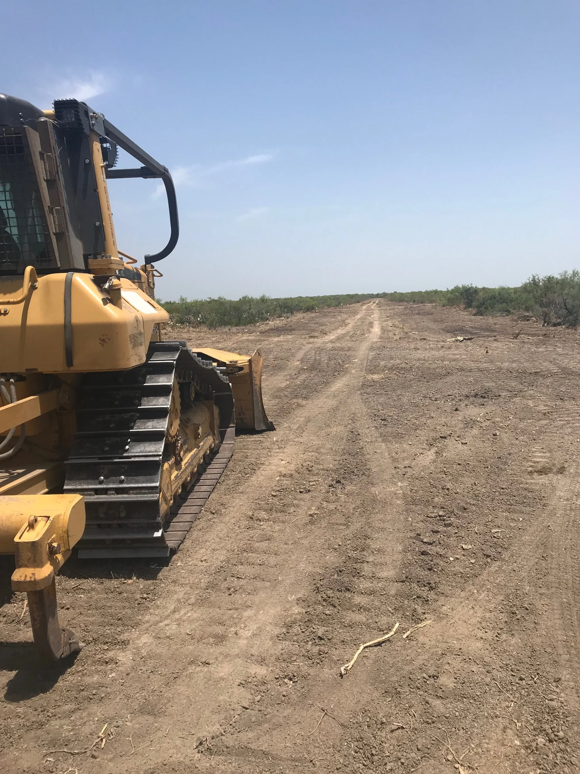 A yellow bulldozer parked on a dirt road with a clear blue sky and sparse vegetation in the background.
