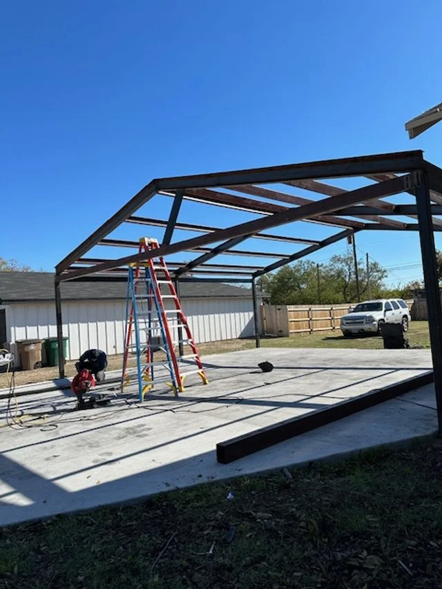 APEX LAND & CONSTRUCTION WEST TEXAS | OZONA | SONORA 76943  Construction site of a carport with a steel frame over a concrete slab, with a red ladder, tools, and a white SUV parked in the background.