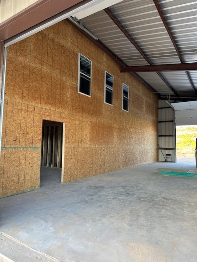 APEX LAND & CONSTRUCTION WEST TEXAS | OZONA | SONORA 76943  Interior view of a partially built wooden structure with three window openings and an open doorway, inside a large metal building with a concrete floor.