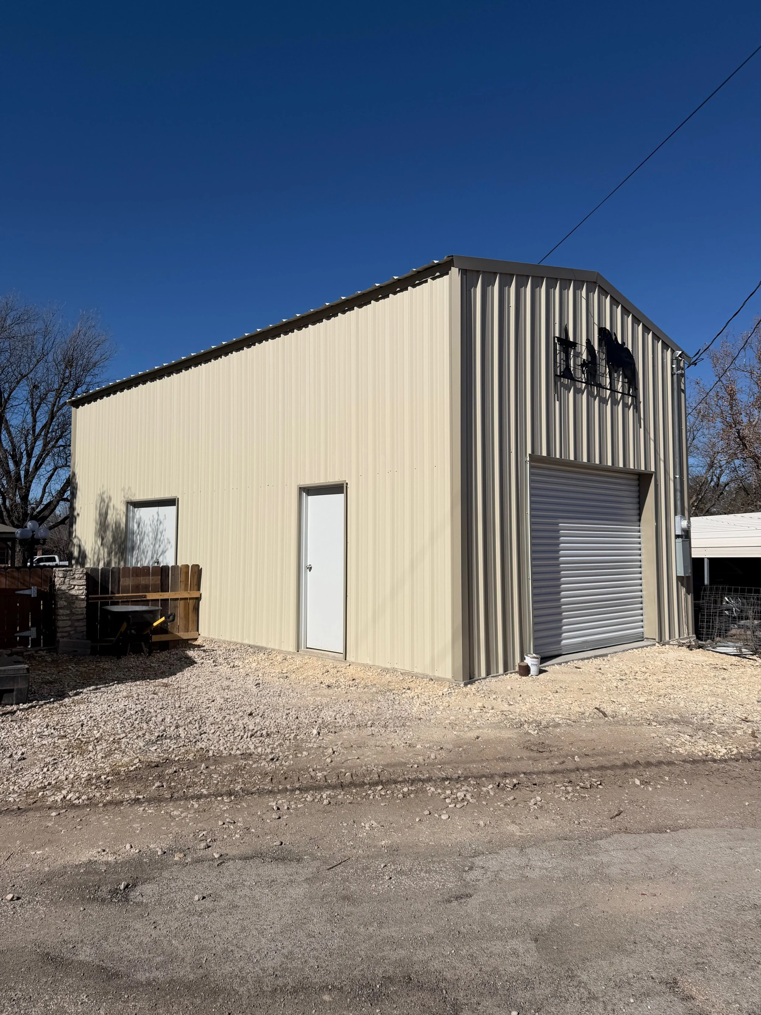 A beige metal building with a roller door and a small plain door, with a sign featuring a horse and rider on the front, under a clear blue sky.