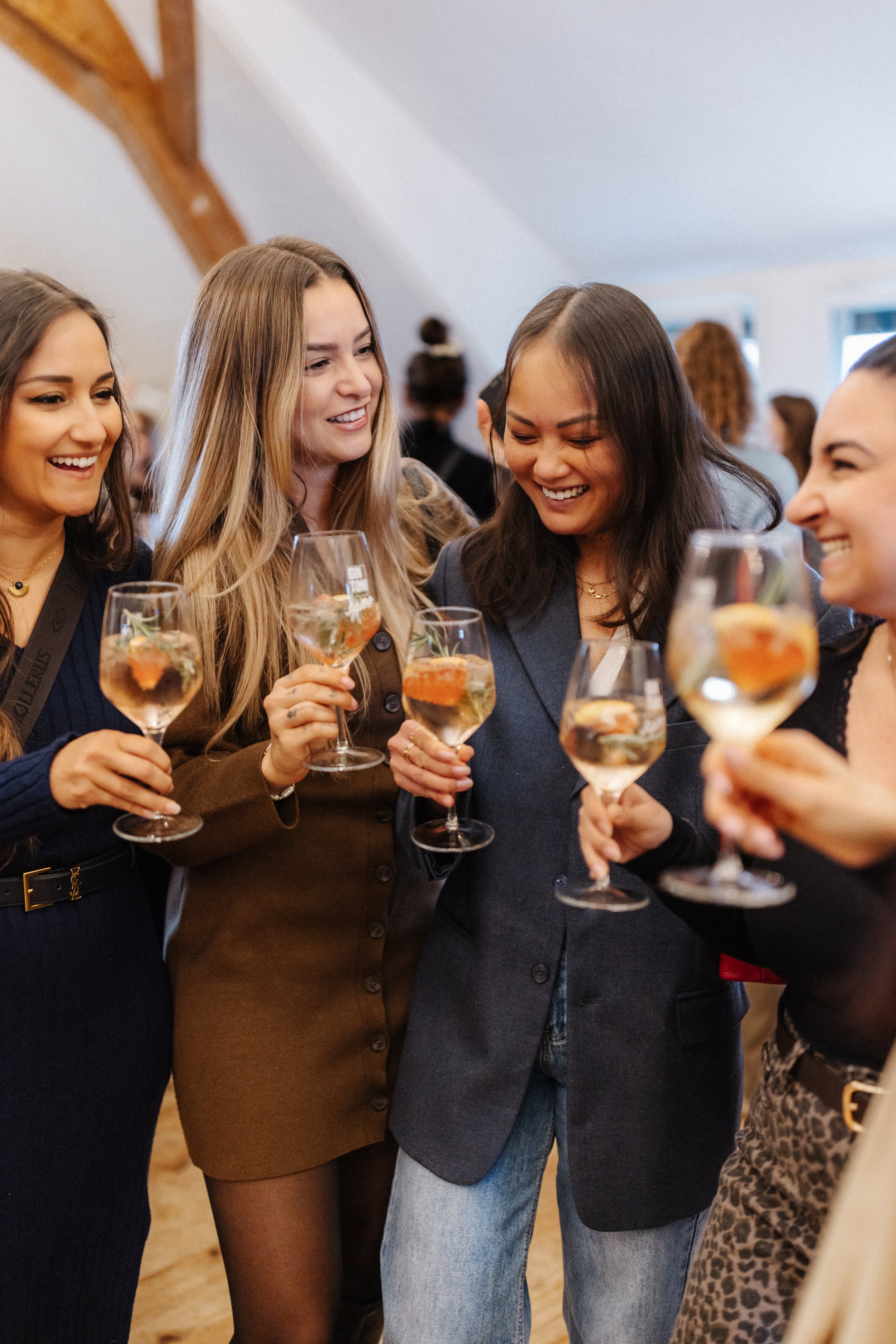 Gruppe von Frauen, die bei einer Feier mit Weingläsern lachen und anstoßen.