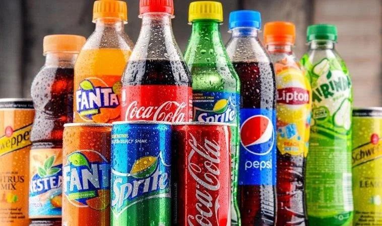 A variety of bottled soft drinks including Coca-Cola, Pepsi, Sprite, Fanta, and other brands on a shelf.
