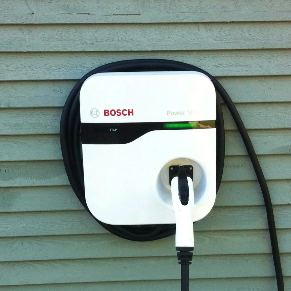 Prise de courant pour véhicule électrique Bosch avec câble de chargement connecté, fixé à un mur en bardage horizontal.