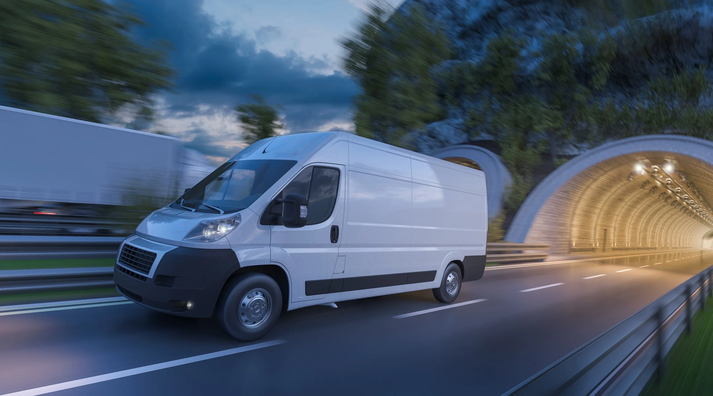 A white delivery van speeds along a highway, exiting a brightly lit tunnel at dusk.